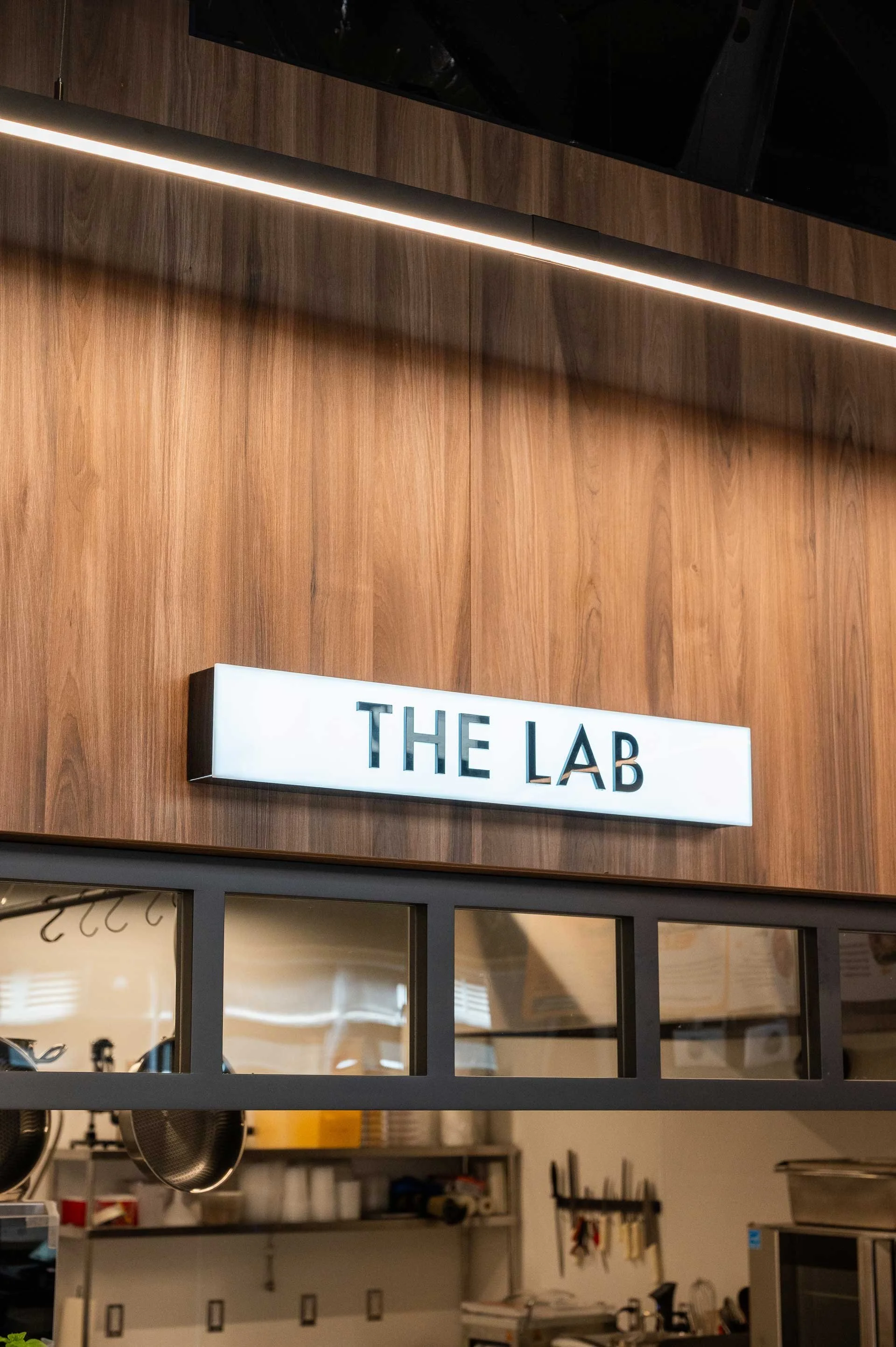 THE LAB illuminated sign on a wood clad wall above a black mullion window