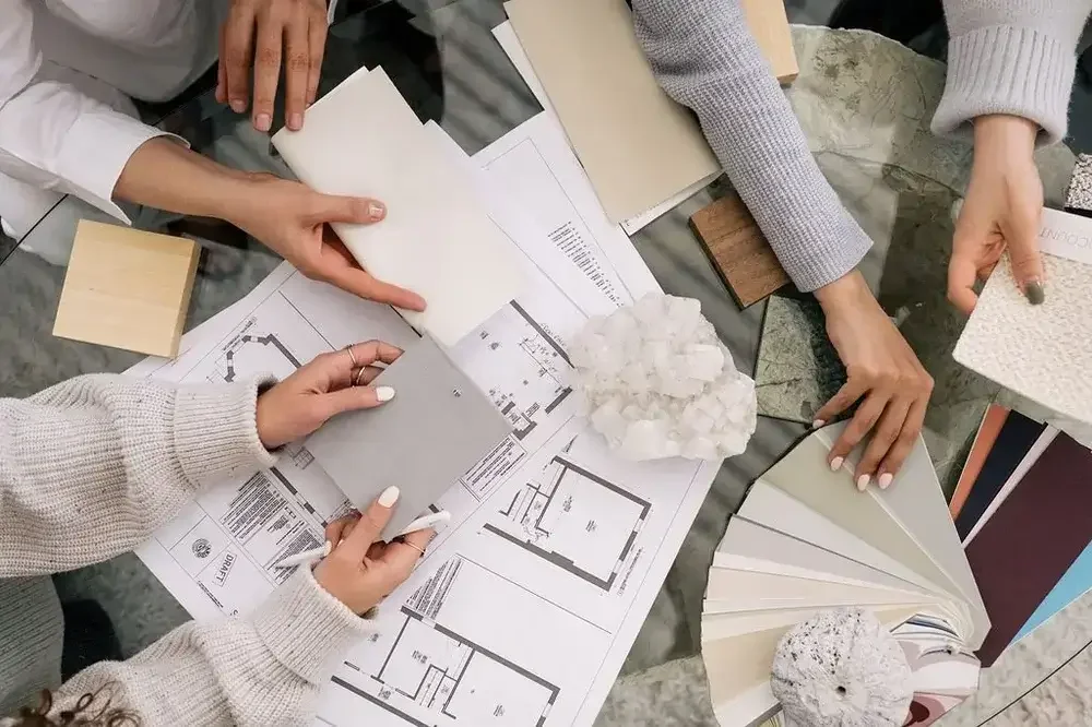 People looking at interior design samples and floor plans on a table, discussing materials and colors.