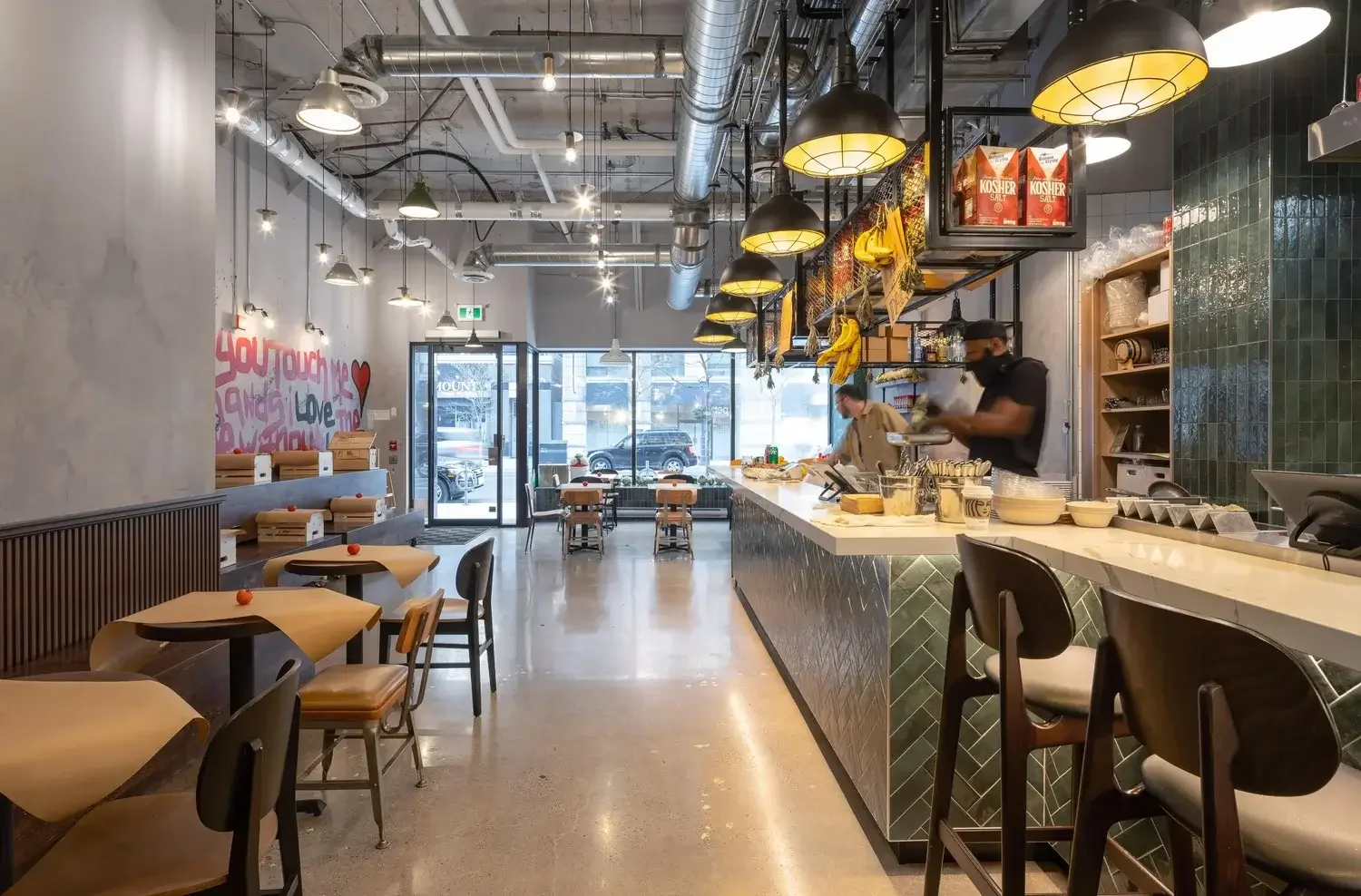 Miznon restaurant interior design in Toronto featuring open kitchen layout, industrial lighting, and bar seating