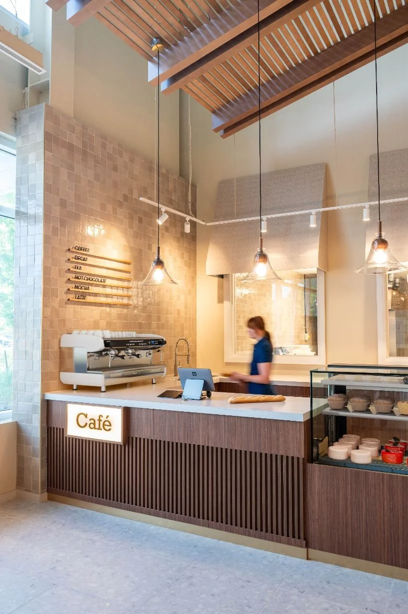 Woman holding bread behind cafe custom check out counter with a large espresso machine and wood slat details