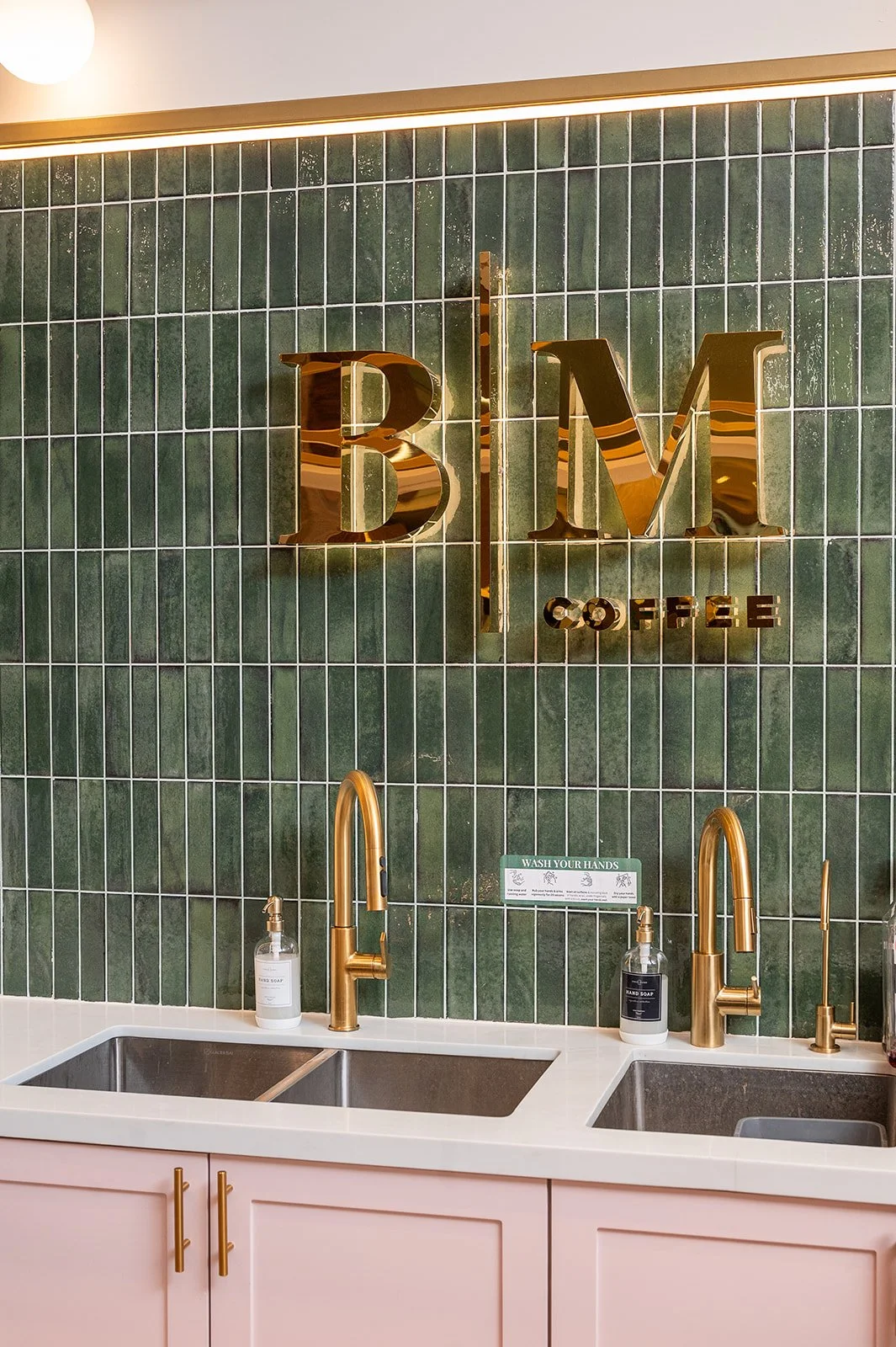 Gold BM logo signage on green tile above pink seating with marble bistro table at Blossom Moments Scotia Plaza
