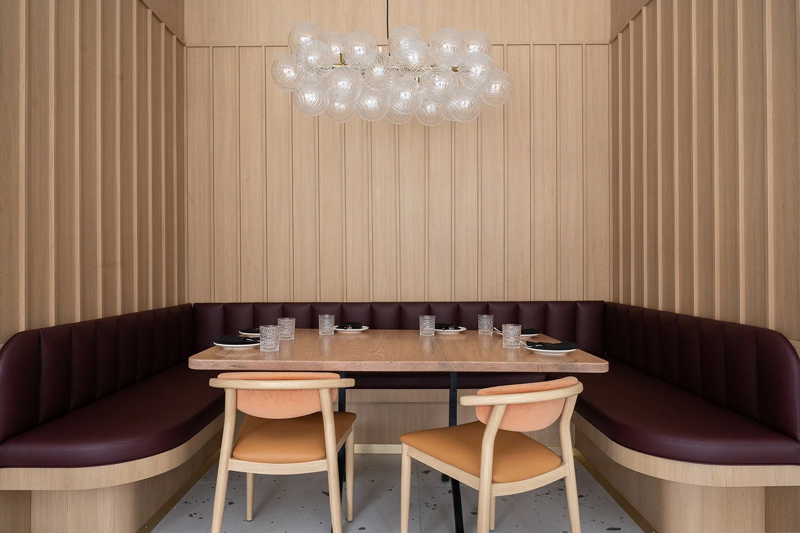 U-shaped booth in Italian restaurant featuring white oak vertical paneled walls, burgundy leather fabric, and glass bubble pendant above
