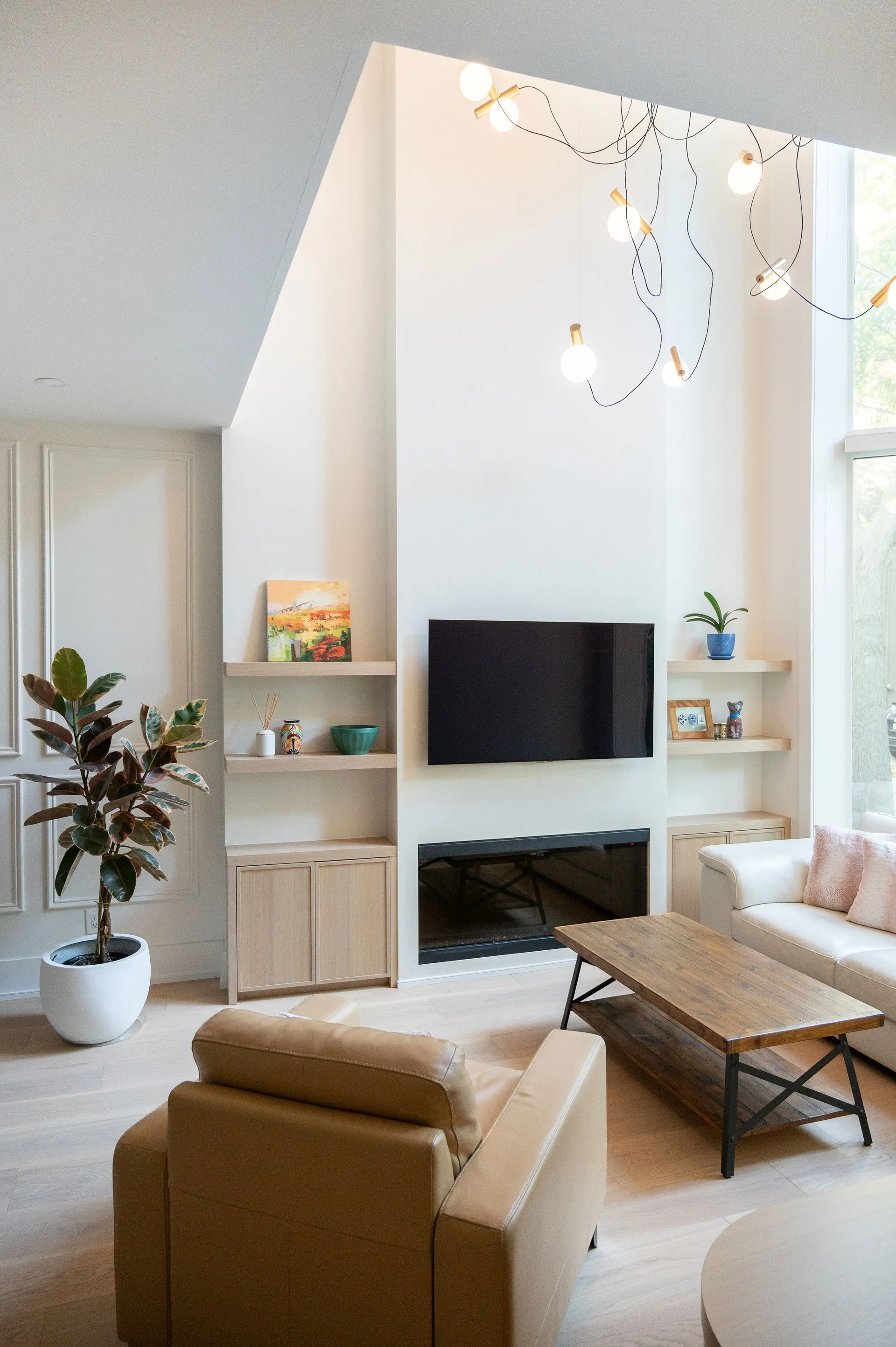 Wall mounted TV over fireplace with white oak cabinetry beside and feature globe light above