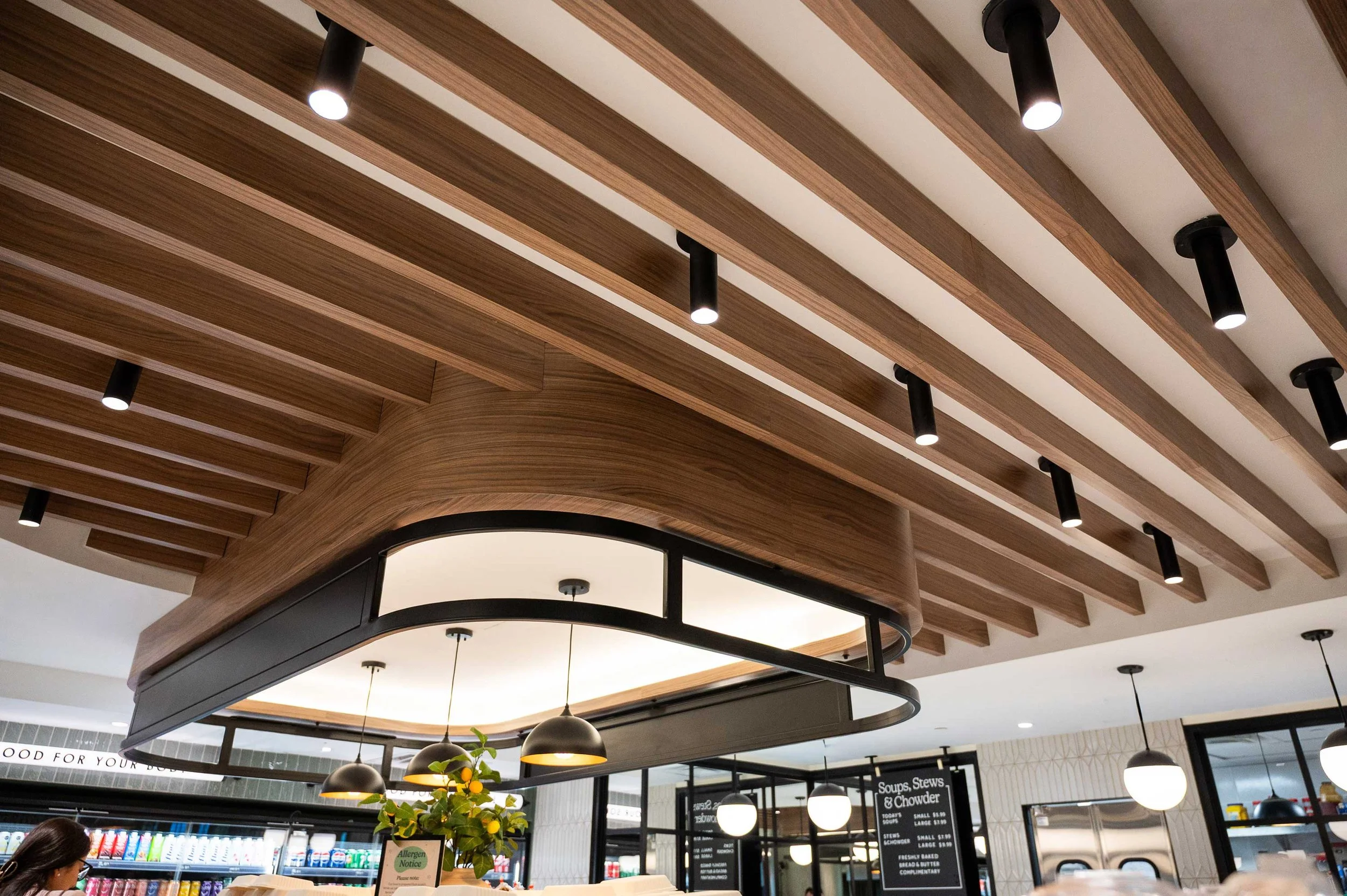 Walnut wood slat ceiling detail with black tubular flush mount lighting
