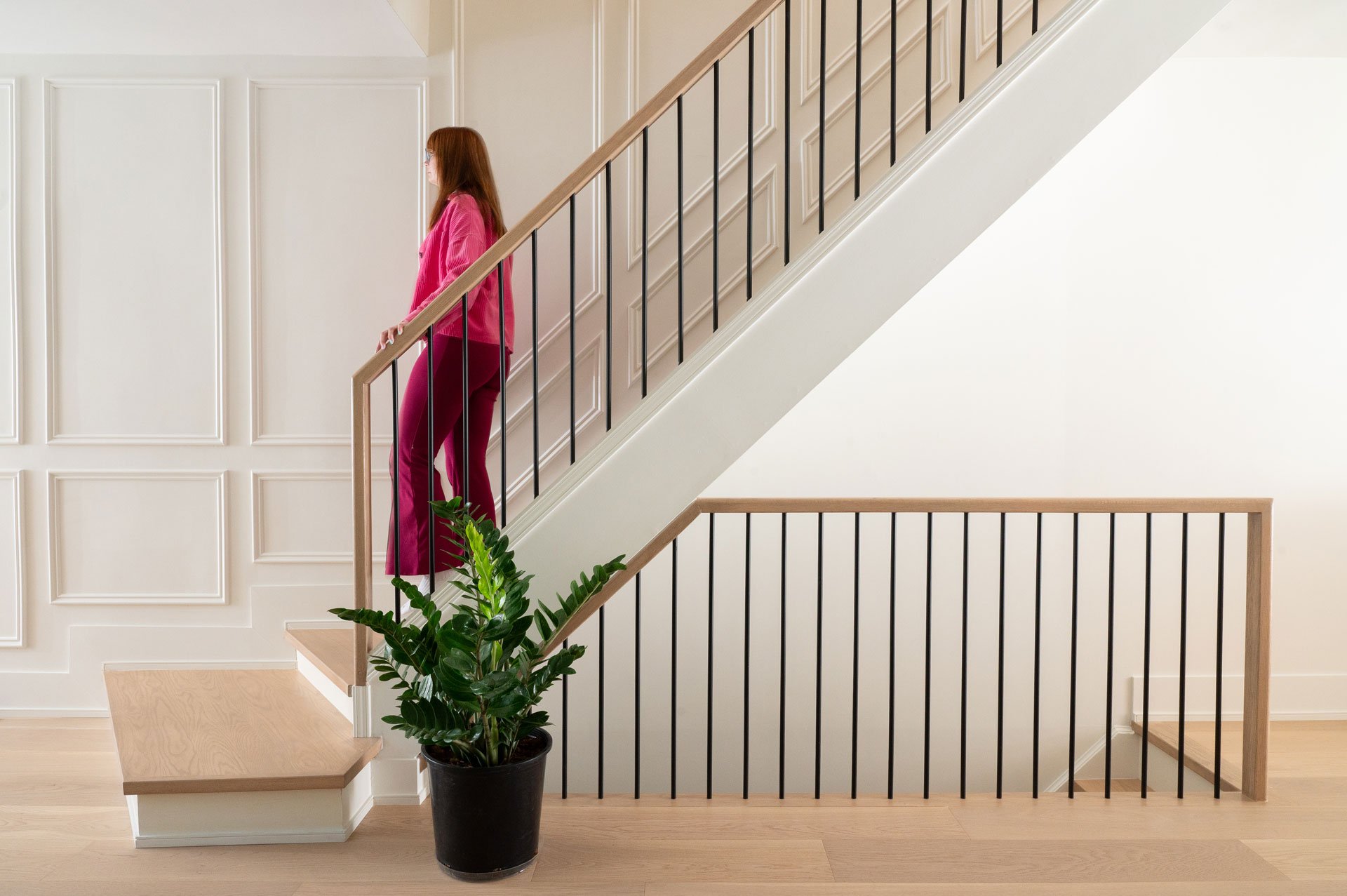 Woman walking down a white oak stair case with white wall moulding behind.