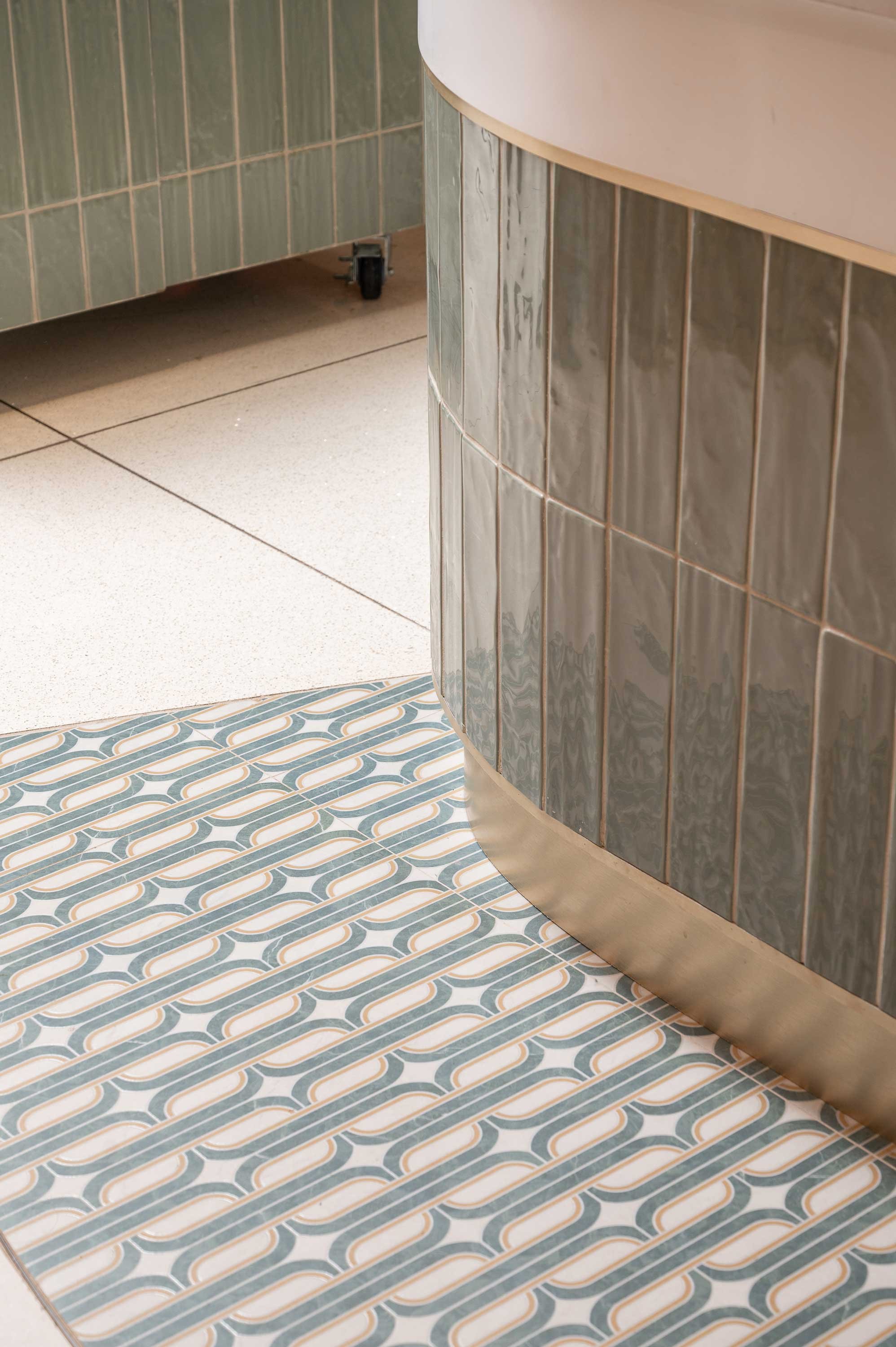 Geometric green tile floor inlay around counter brass base 