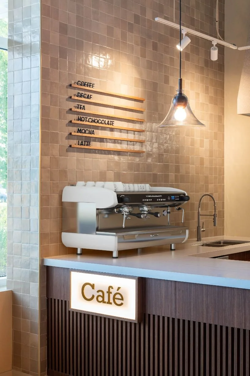 espresso machine on top of custom cafe counter with a tiled wall and menu board above