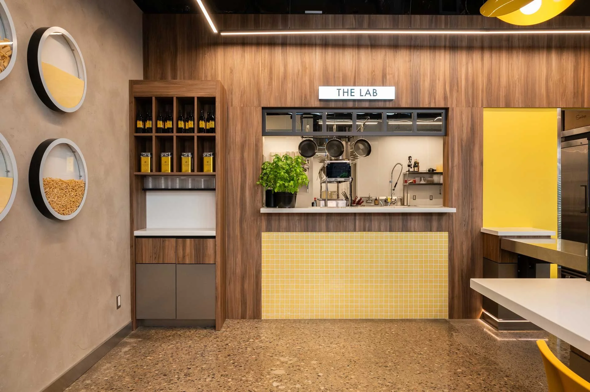Restaurant passthrough window with illuminate THE LAB signage above. Wood walls and yellow mosaic tile with condiment station next to it