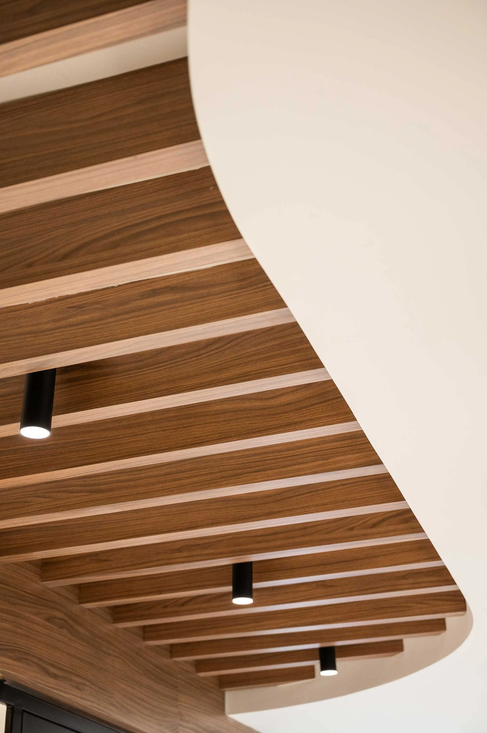 Walnut wood ceiling slats connecting to curved drywall bulkhead 