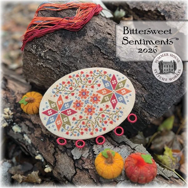 Bittersweet vine and star motif cross stitched floss board sitting on log in autumn scene with wool felt pumpkins.