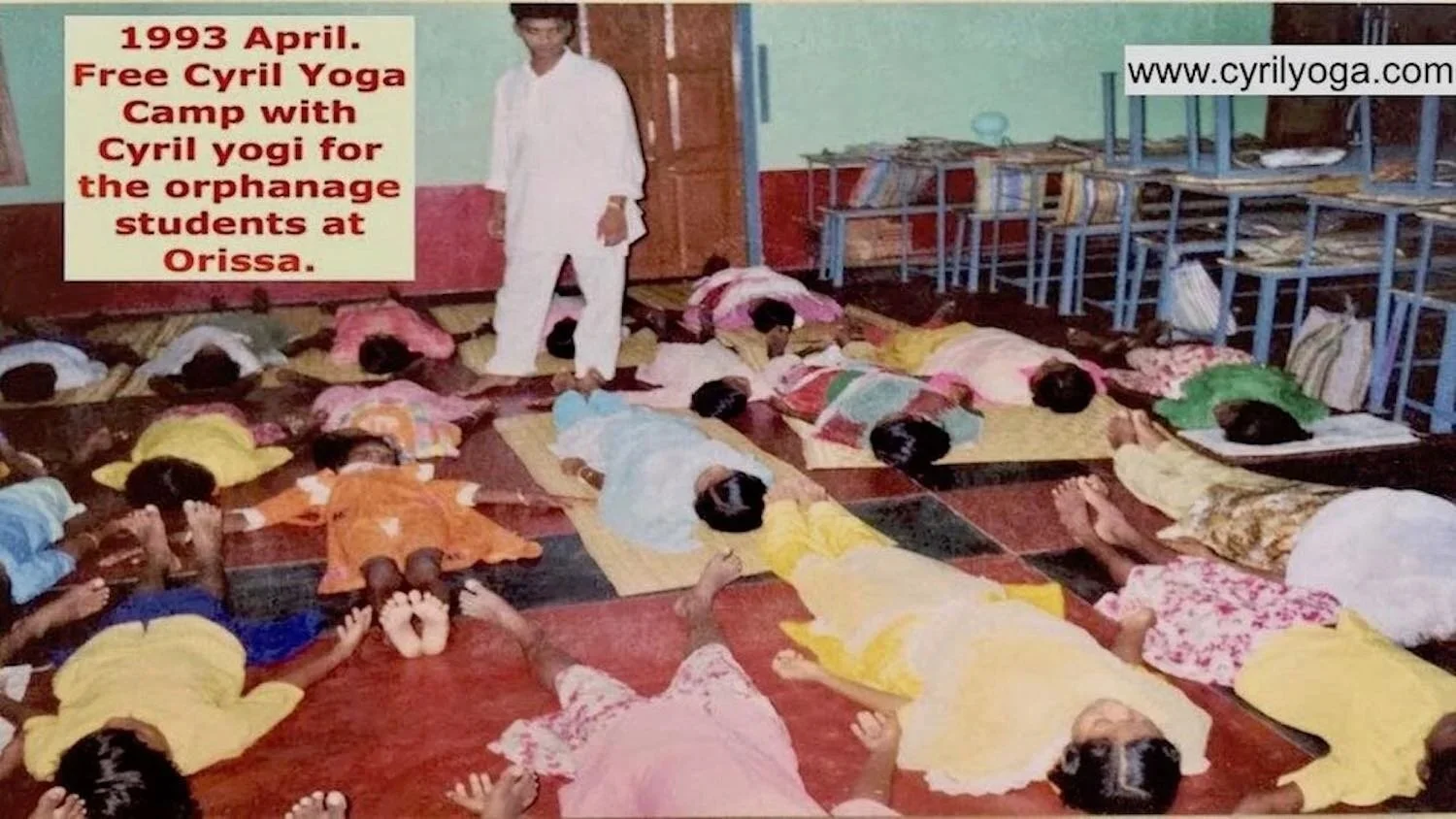 Children lying on mats and pillows on the floor in a classroom, attending a yoga camp led by a man standing in white clothes. Colorful walls and metal shelves with books are visible in the background, dated April 1993.