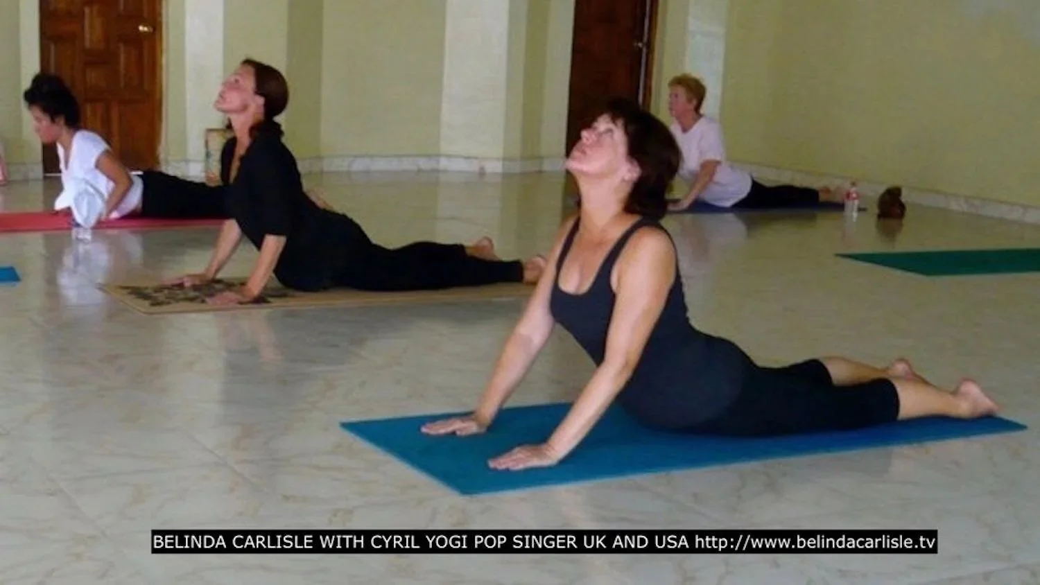 Group of women participating in a yoga class, performing upward dog pose on yoga mats in a spacious room.