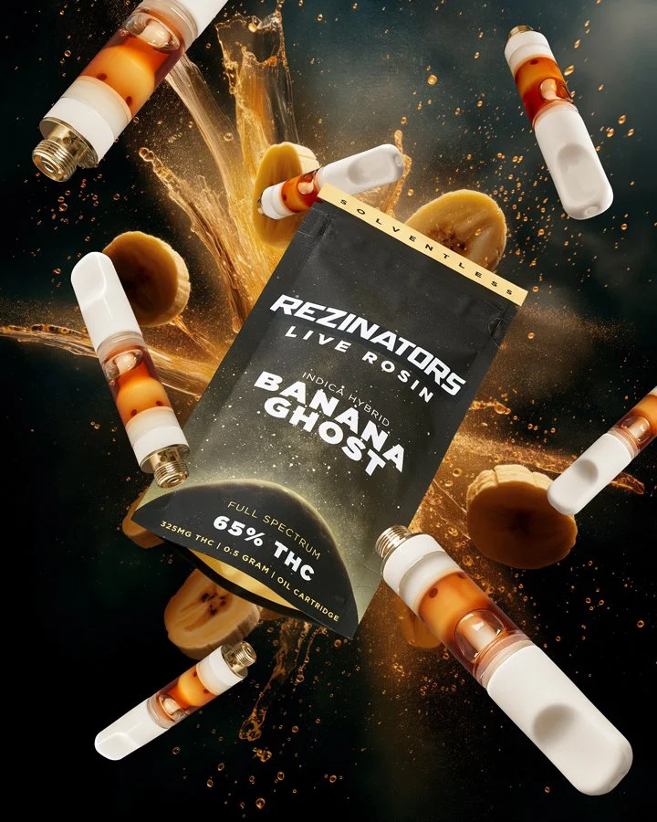 A package of Rezinator live rosin cannabis extract surrounded by several vape pens and cannabis cookies, with a splash of liquid and a dark background.