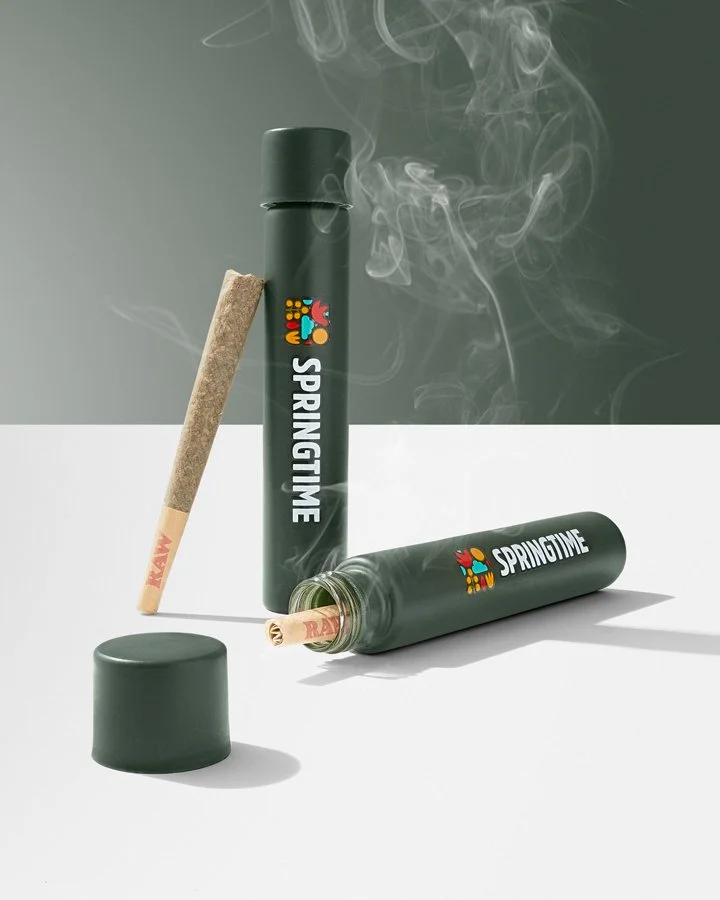 Two green cylindrical containers labeled 'Springtime', one open with a joint inside, and a third closed container with a joint leaning against it, along with a lit joint emitting smoke on a white surface.