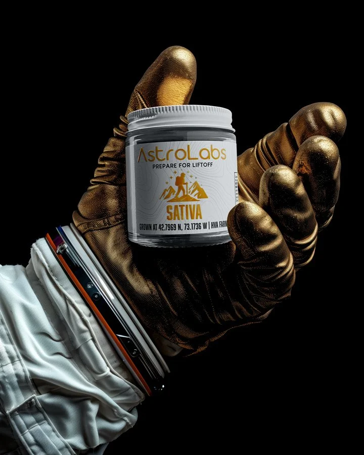 A hand wearing a black and gold glove holds a container labeled AstroLabs Prepare for Lift Off, Sativa. The person is dressed in a white astronaut suit with gray and orange accents.