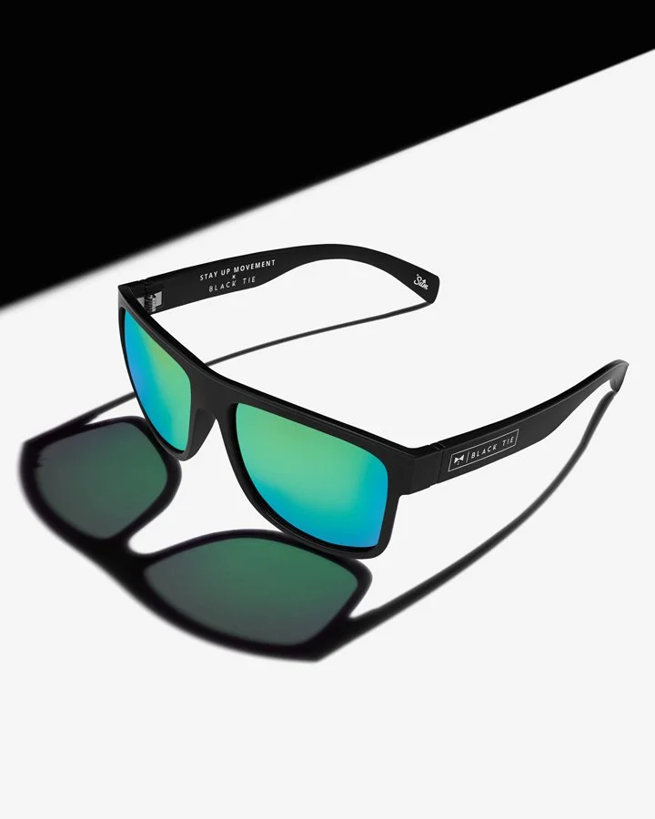 Pair of black sunglasses with reflective green-blue lenses on a black and white background.