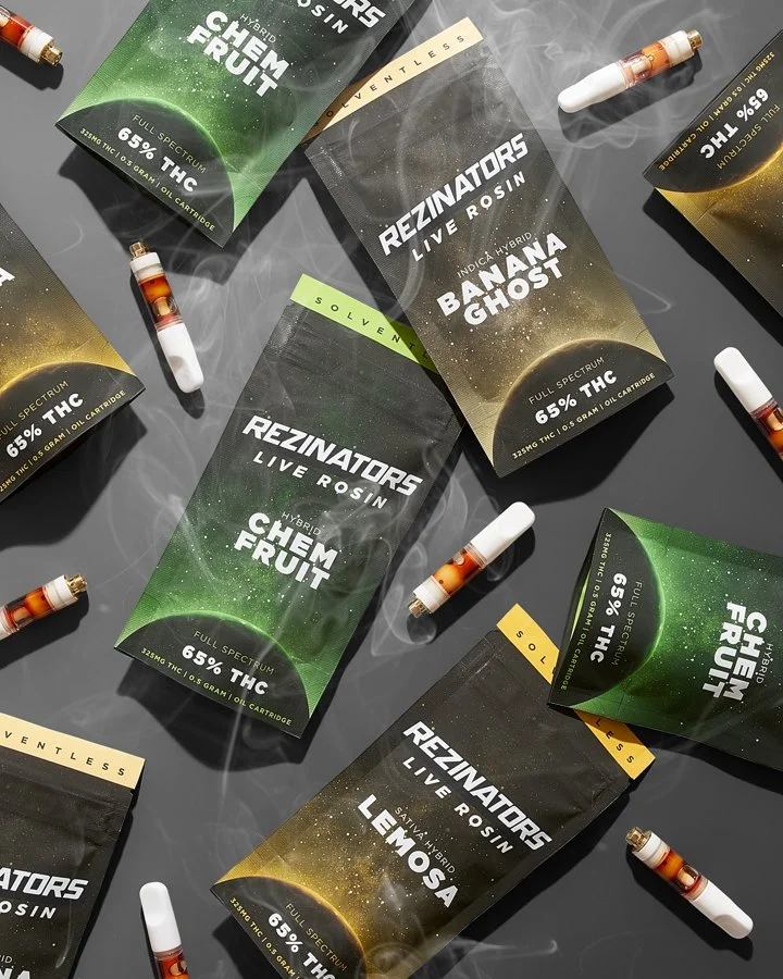 Cannabis vape cartridge packaging with cannabis-themed names and labels, scattered on a dark surface, with vapor clouds.