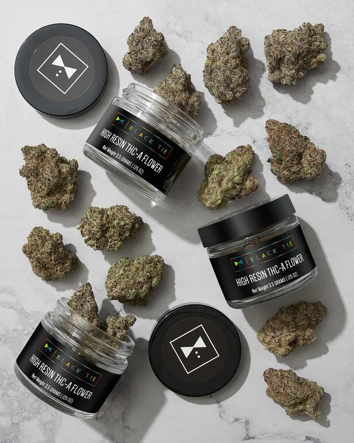 Cannabis buds and containers labeled 'High Resin THC-A Flower' on a light gray surface.