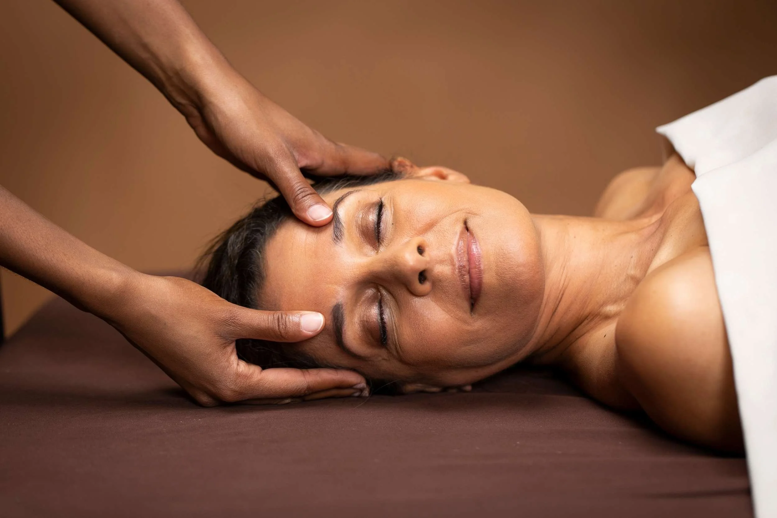 A woman improves her emotional wellbeing by receiving a massage, where the massage therapist gently places her thumbs on the woman's forehead
