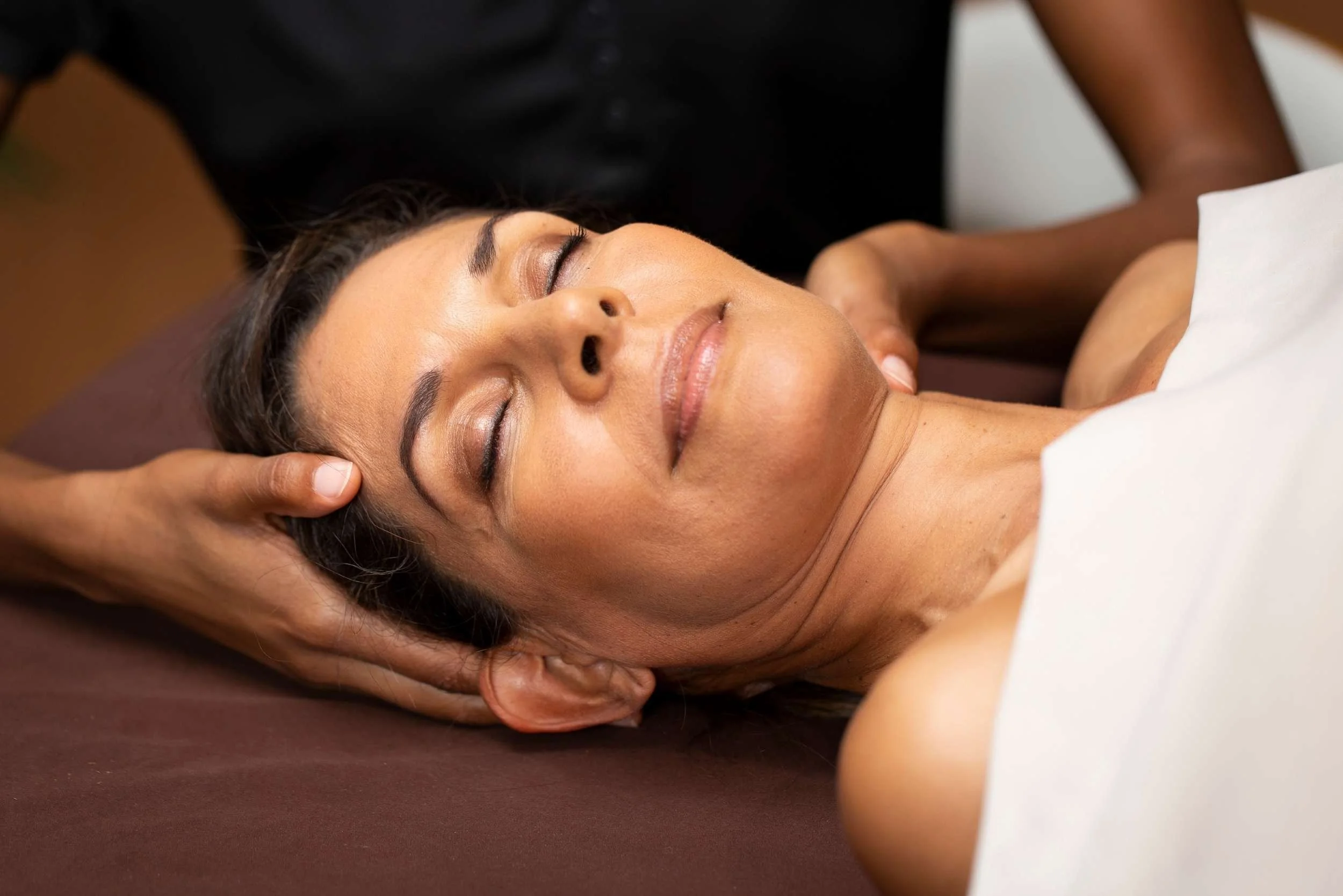A woman with a high stress career relieves stress through massage. She reclines on a massage table as the massage therapist applies pressure to her scalp and neck.