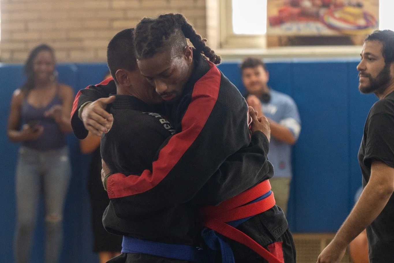 Two Harlem Free Fight Academy students embrace after a match as teammates and coaches cheer