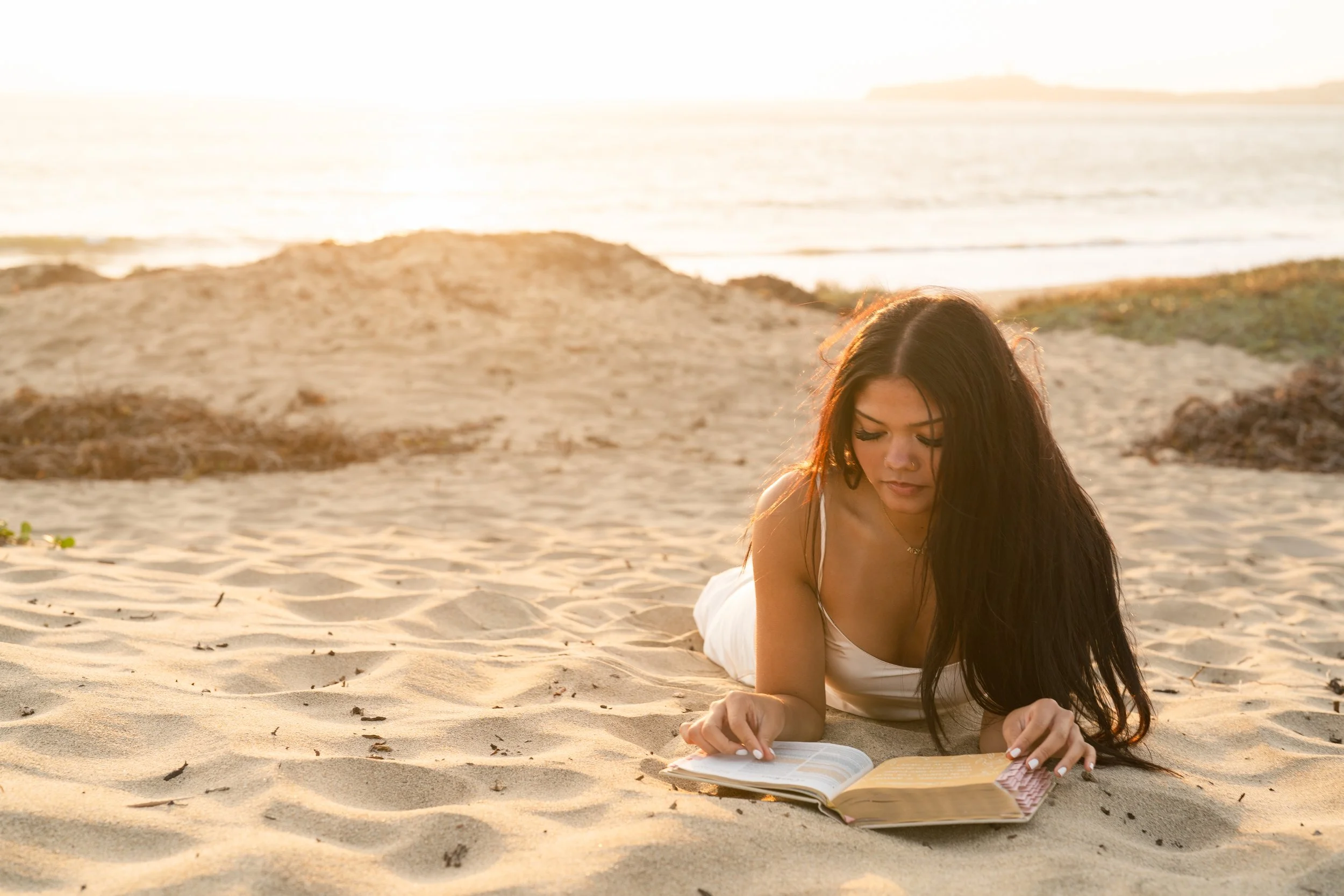 Senior lying in the sand reading her Bible in warm sunset light at a Half Moon Bay beach