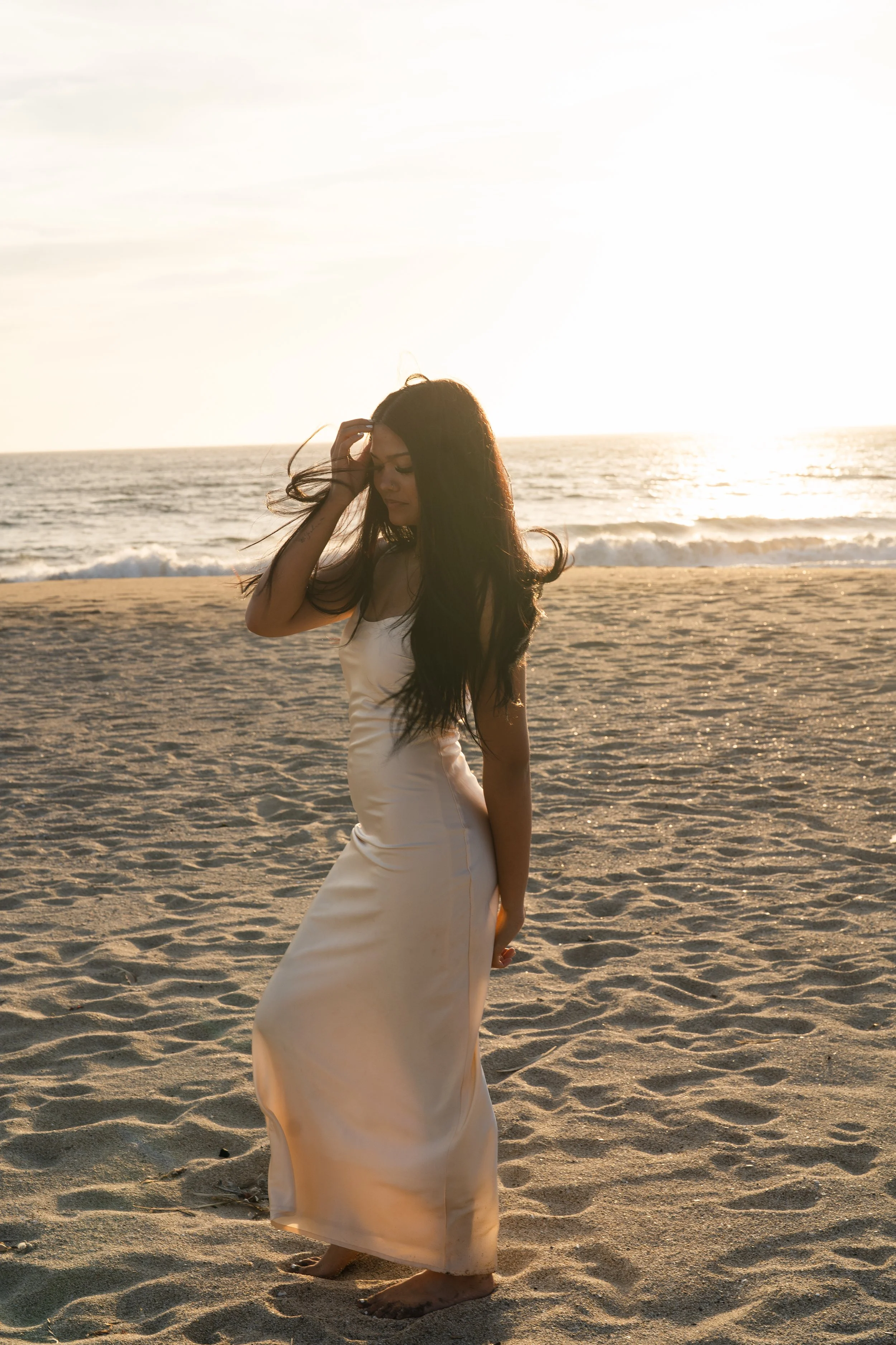 Backlit golden hour senior portrait of a girl brushing her hair back on the sand in Half Moon Bay