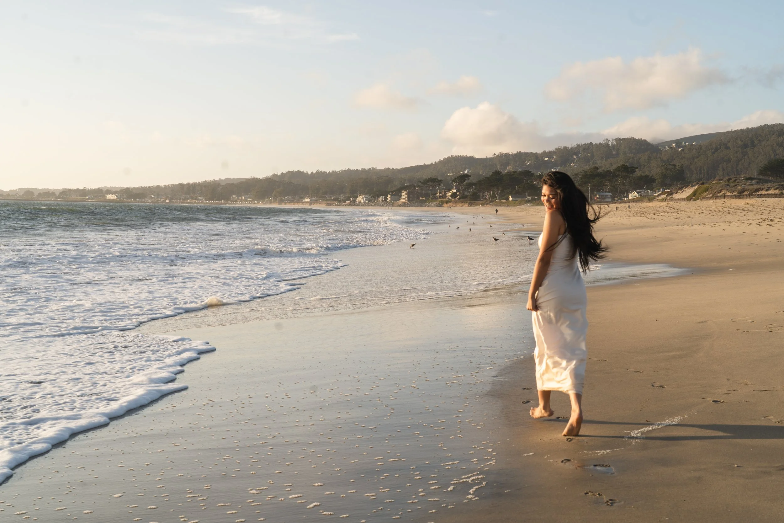 Candid wide shot of a high school senior near the waves, sun glowing over the Half Moon Bay coastline