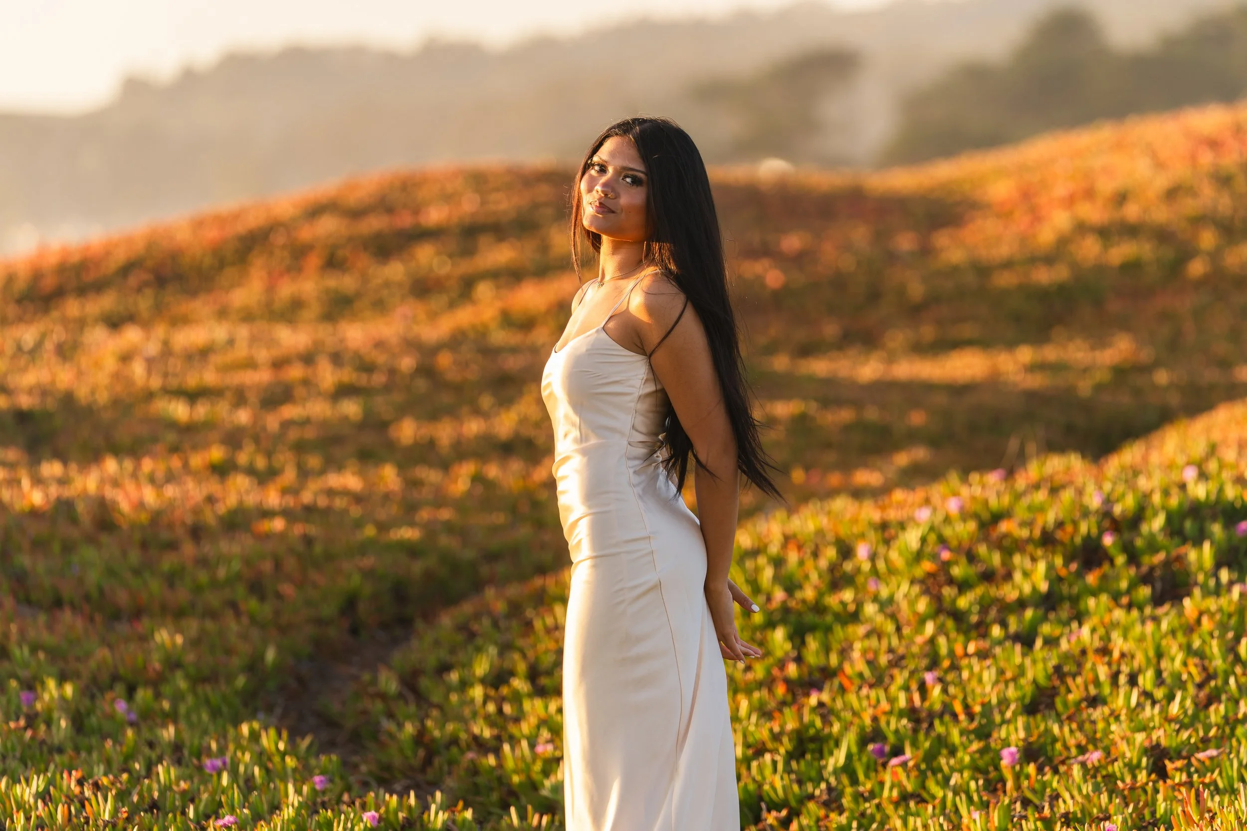 High school senior standing among ice plant on the coastal bluffs, looking back over her shoulder in Half Moon Bay