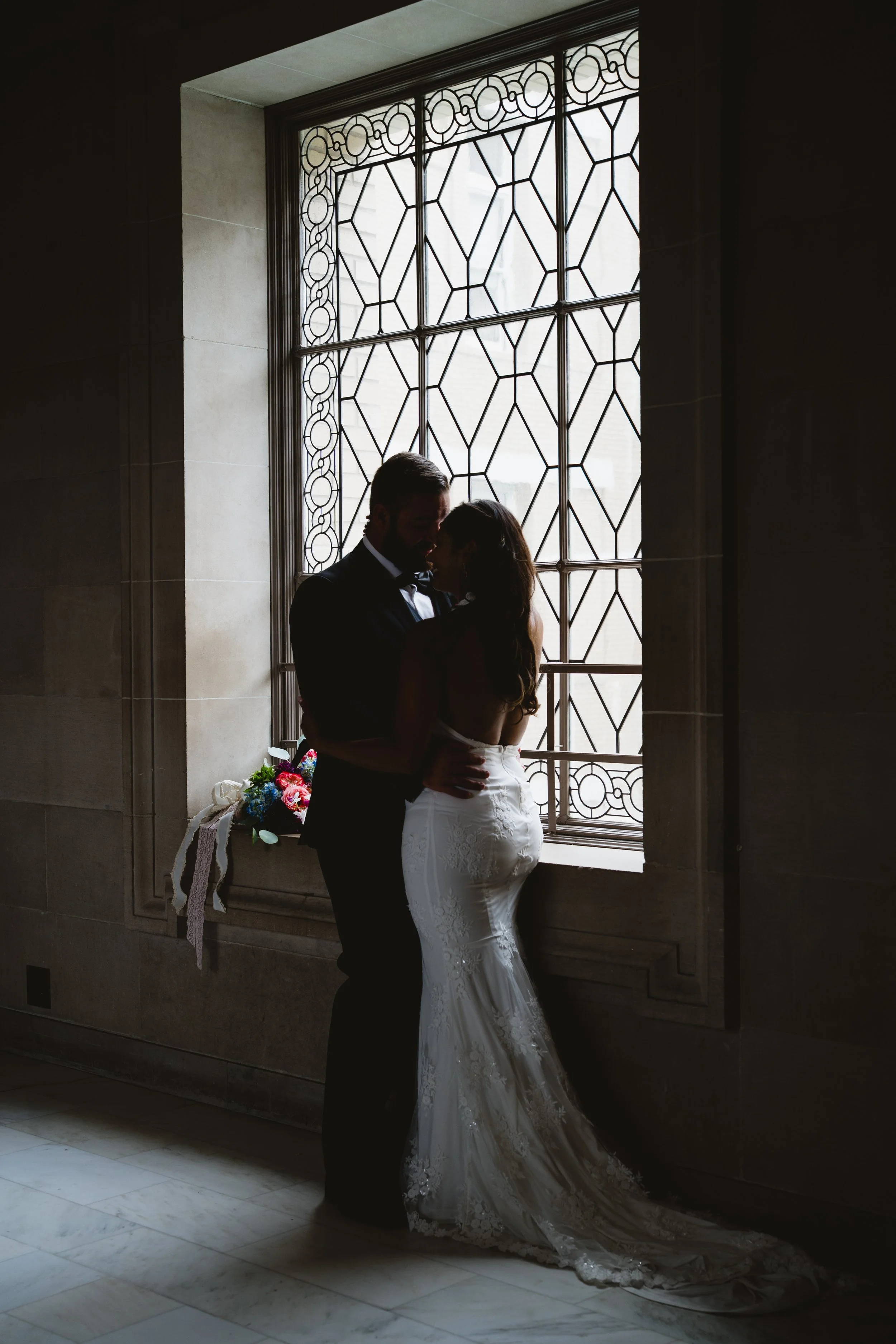 Silhouette of a couple in a close embrace in front of a leaded-glass window.
