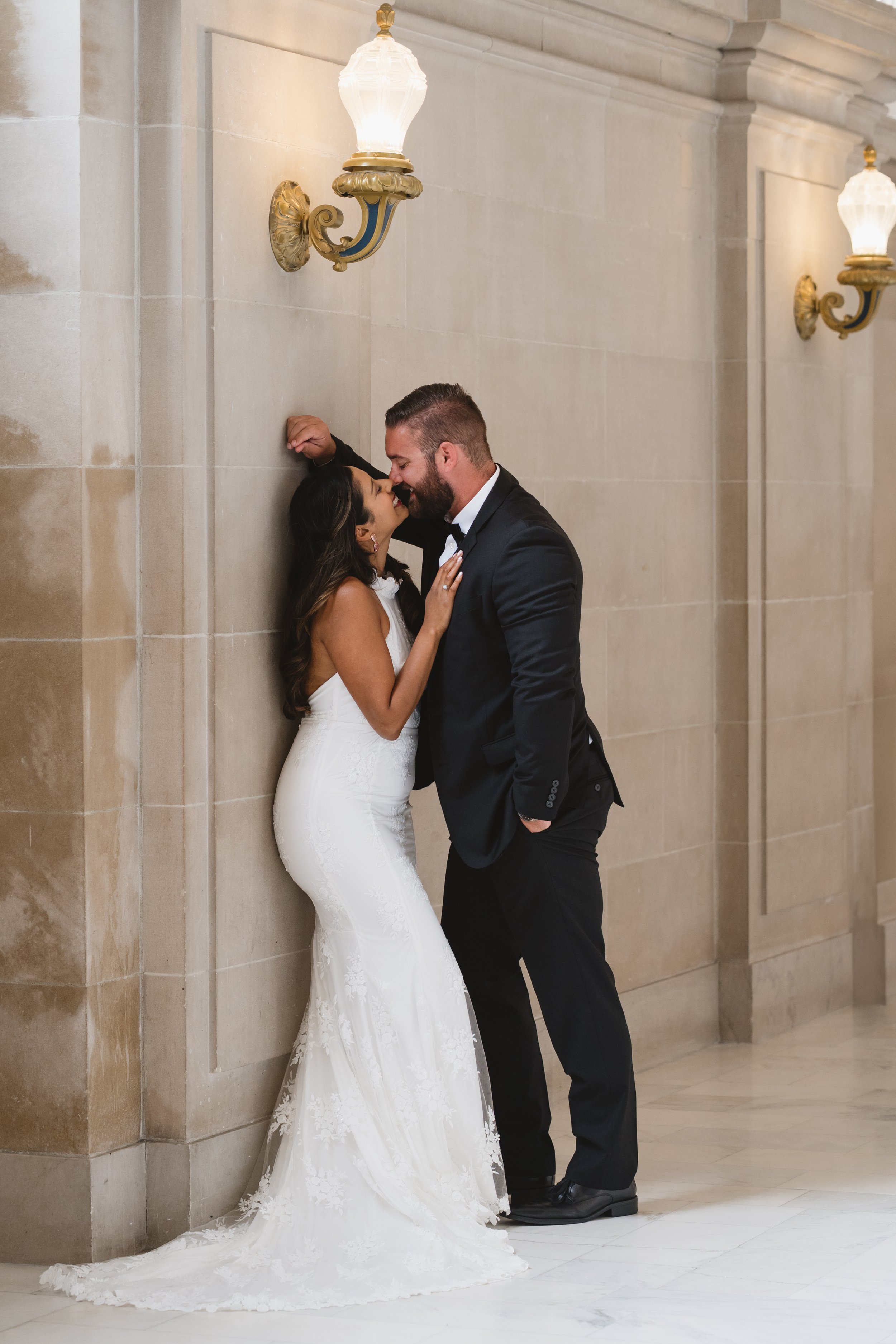 Couple embracing against a marble corridor wall lit by ornate brass wall sconces.