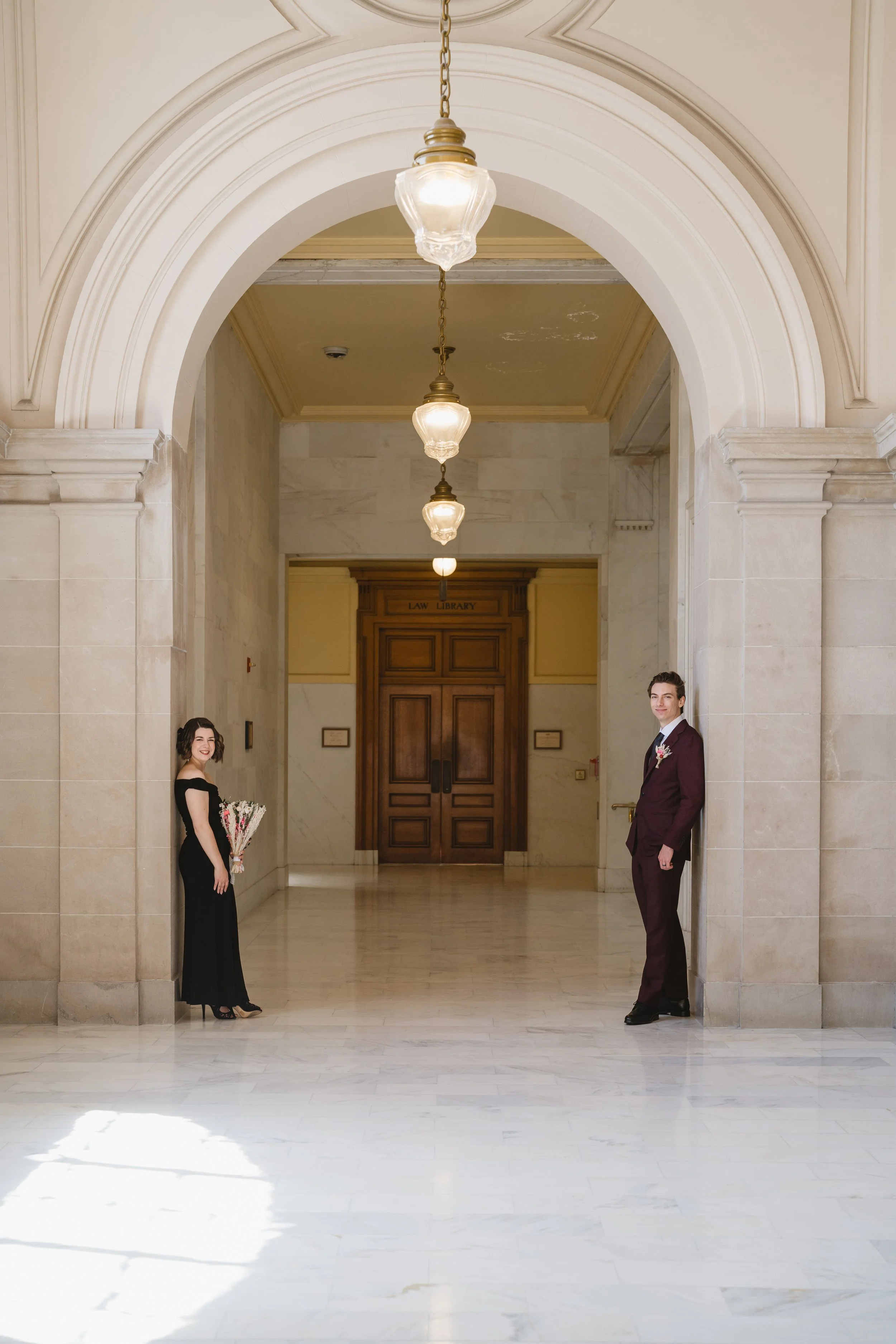 Bride and groom under a marble archway at SF City Hall