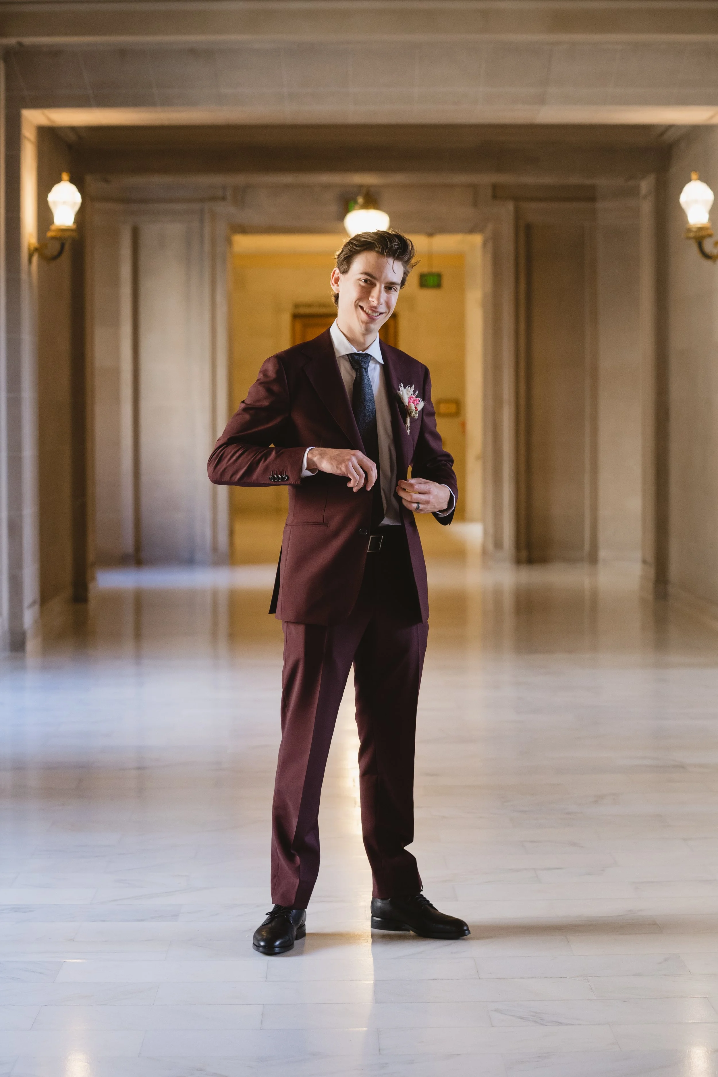 Groom in a burgundy suit in a San Francisco City Hall hallway