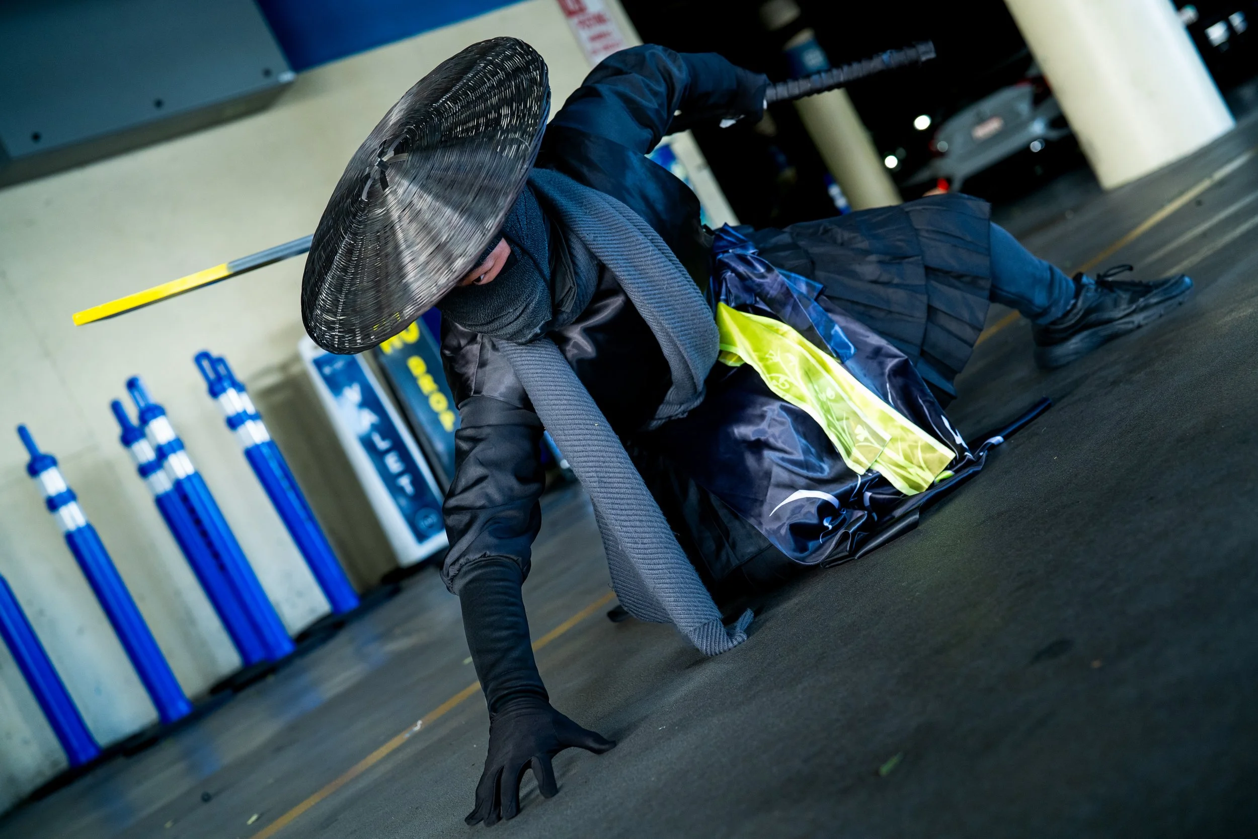 Person dressed in dark clothing with a black mask and large hat, performing a breakdance move on the ground in a parking garage.