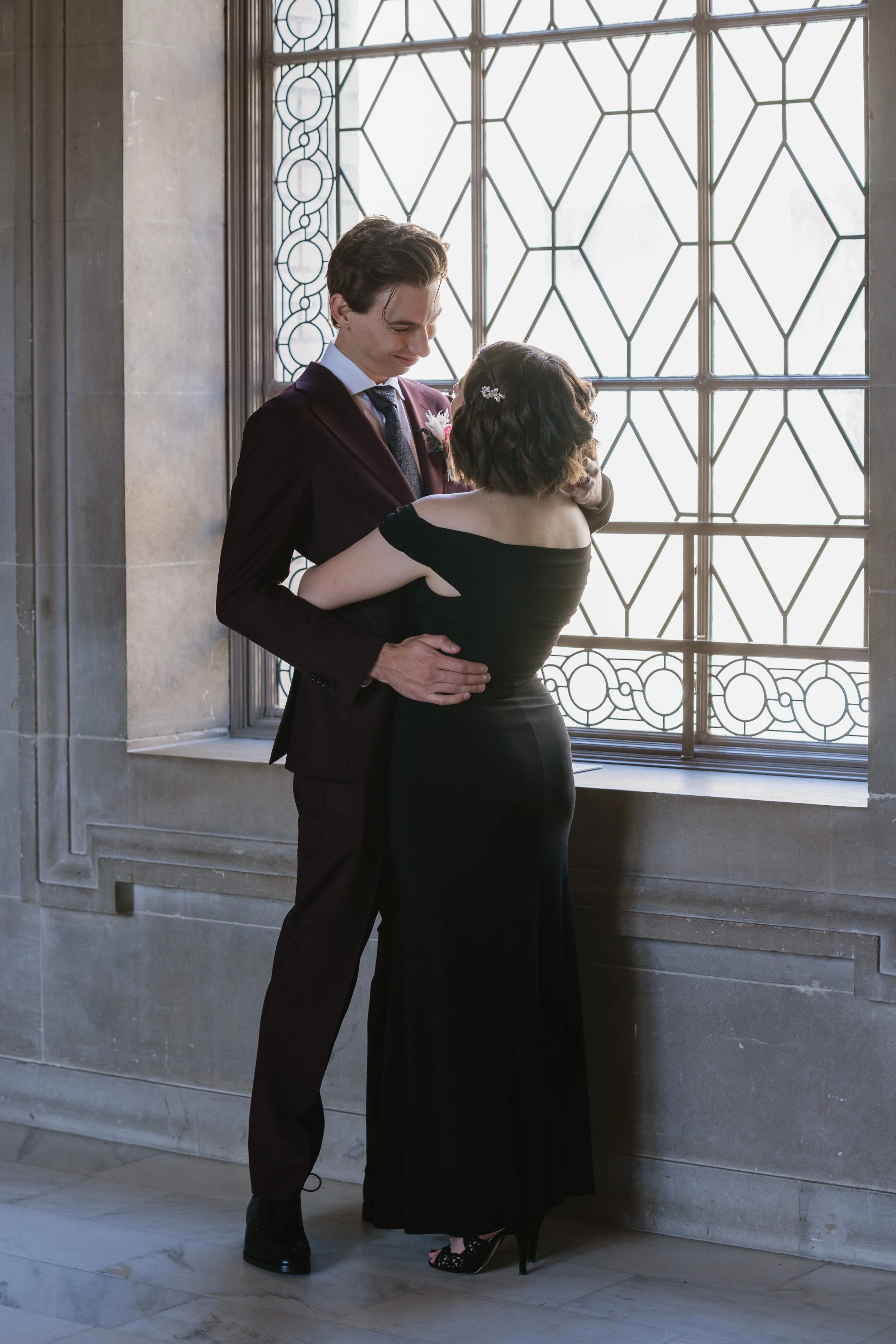Newlyweds embracing by a window at San Francisco City Hall