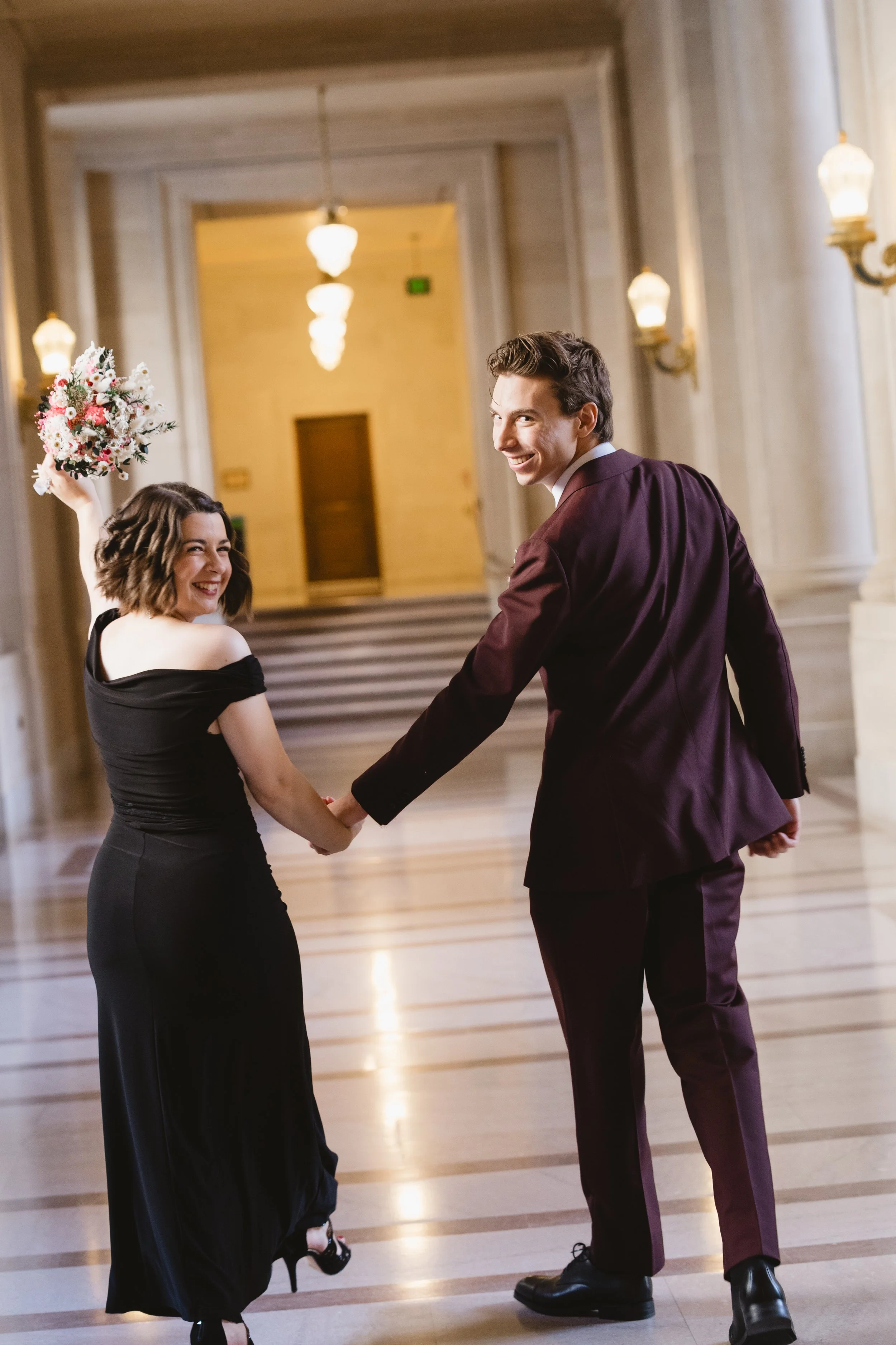 Bride raising her bouquet while walking a City Hall hallway