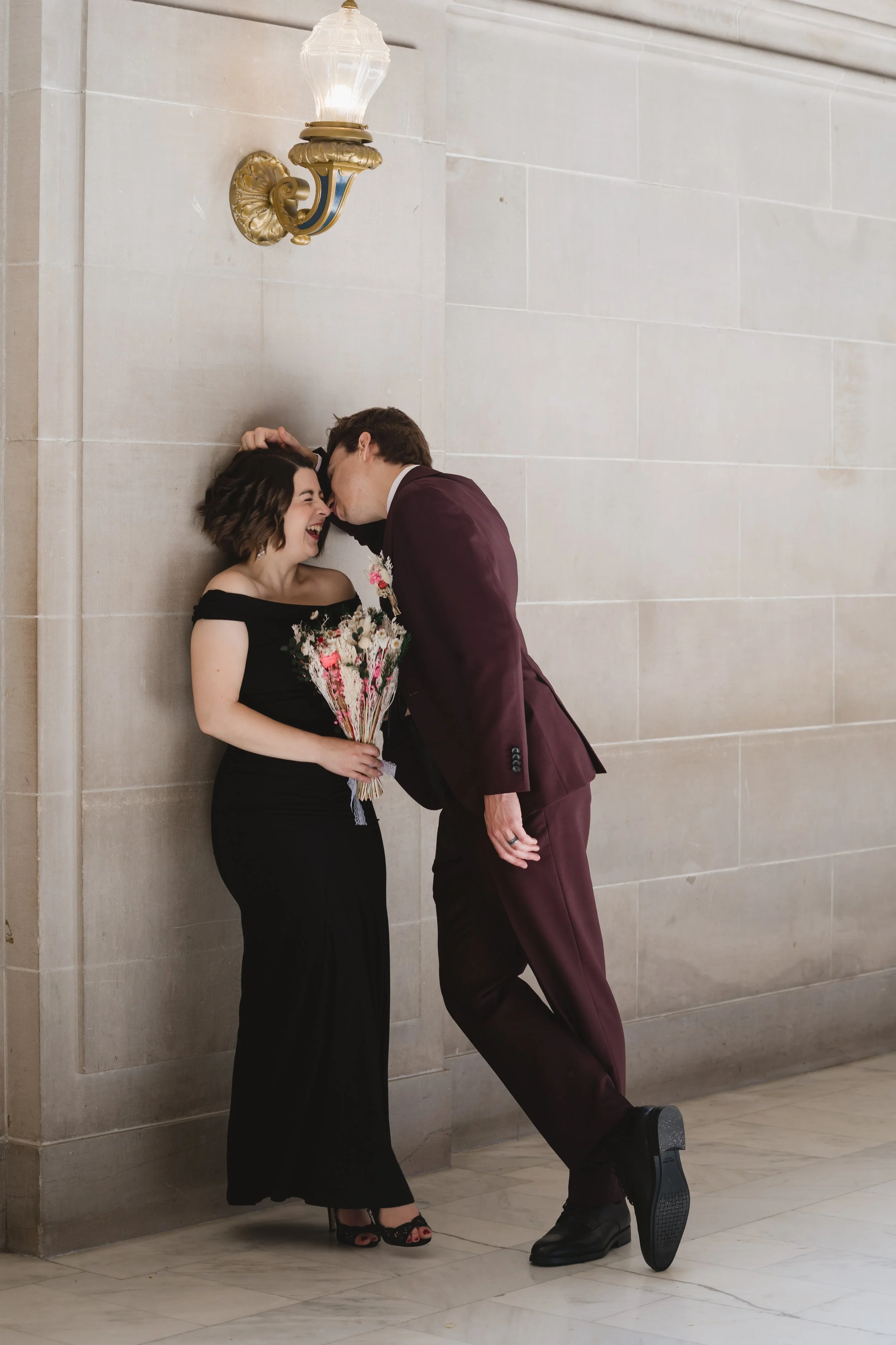 Groom kissing bride's forehead beside a wall sconce