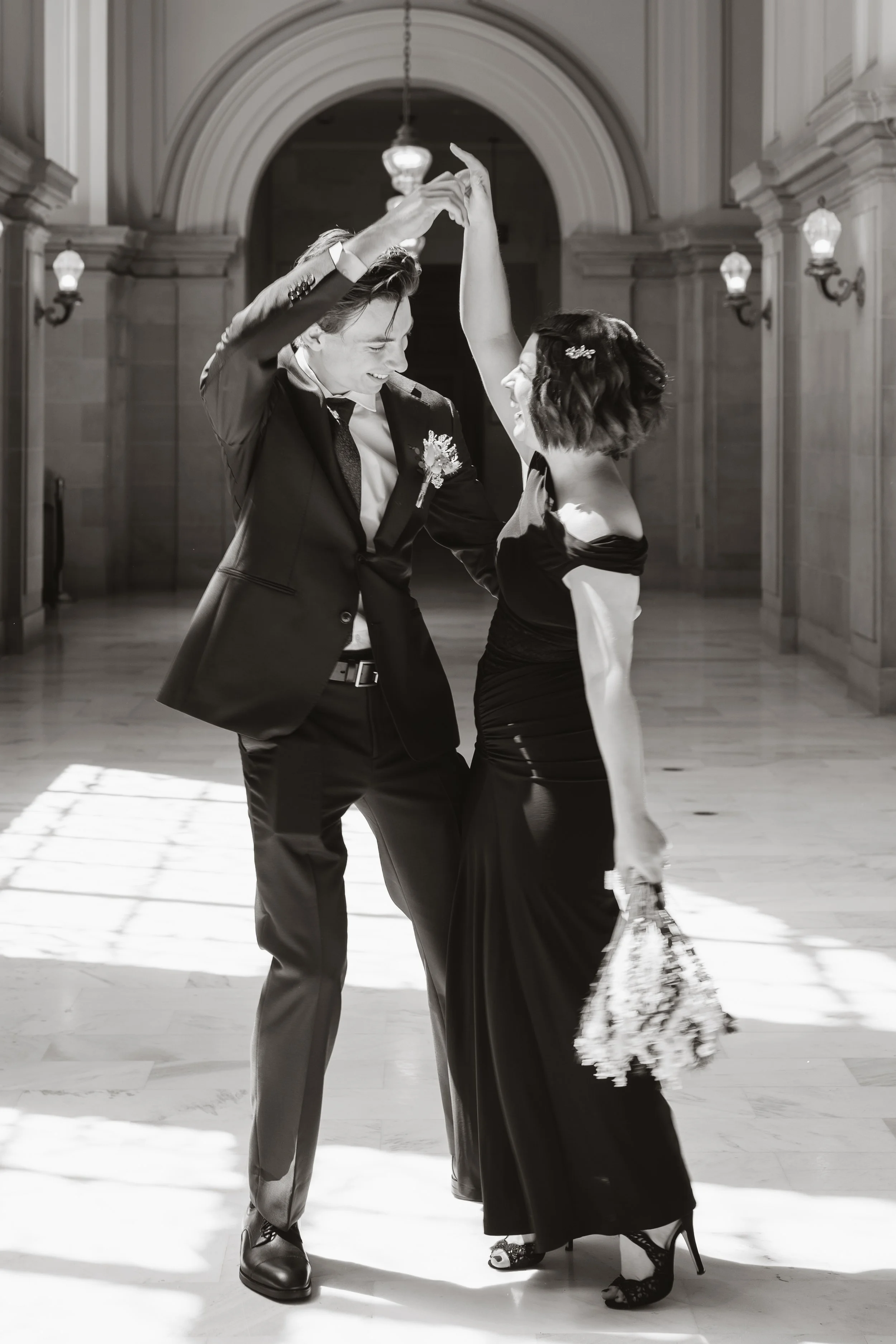 Black and white photo of couple twirling in a City Hall corridor