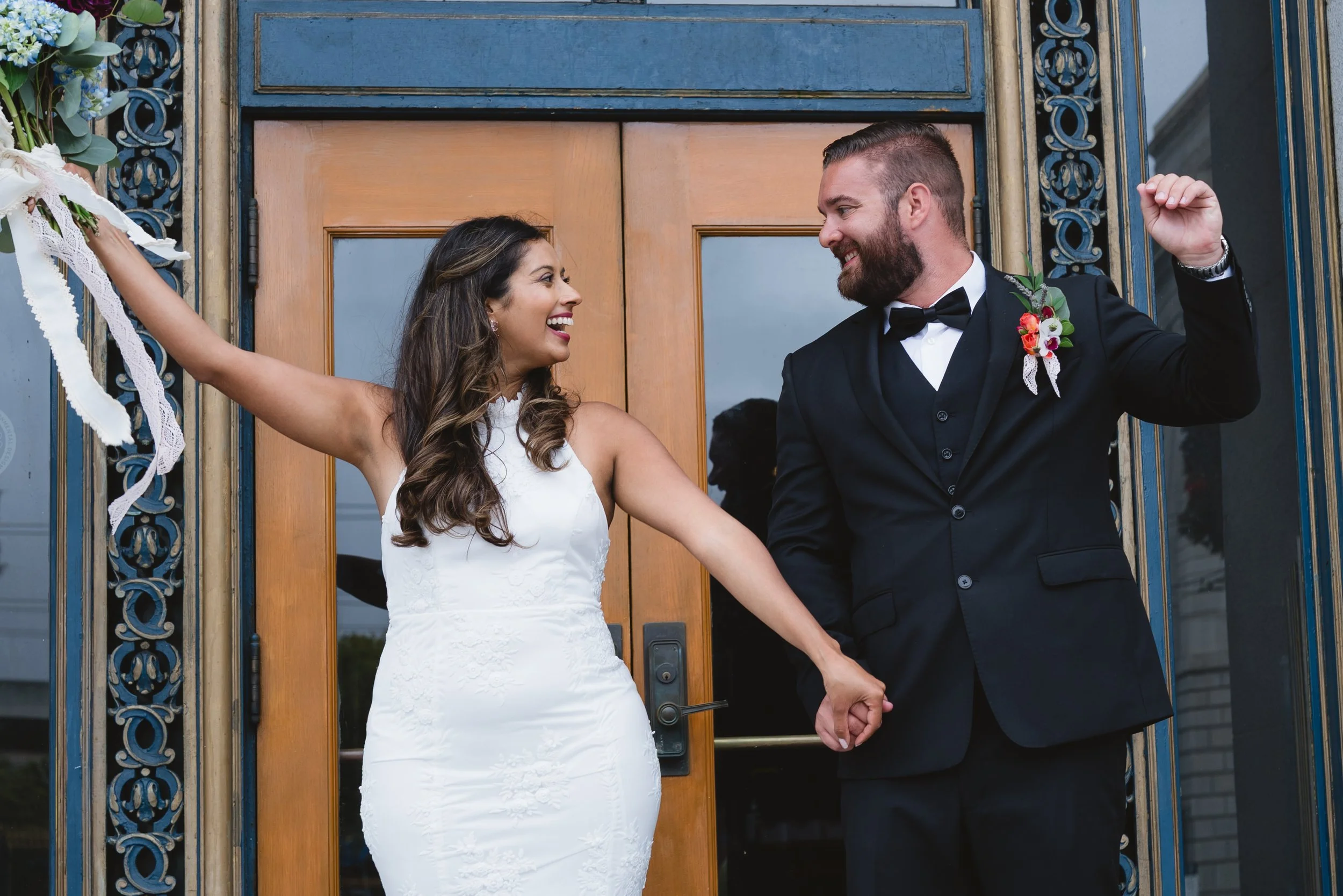 Bride and groom celebrating their marriage in front of San Francisco City Hall Doors. Bride is holding a flower bouquet.