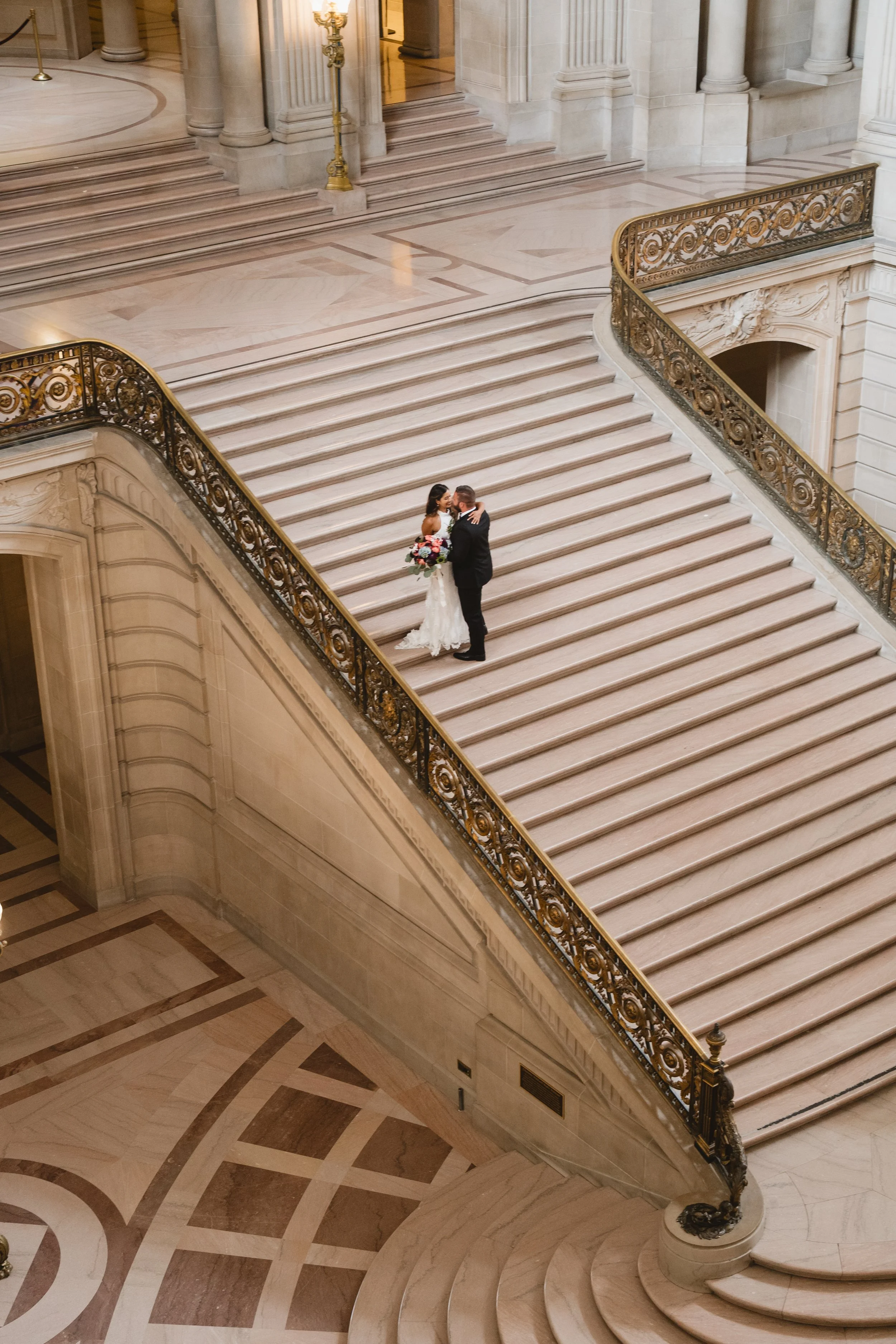 Aerial view of a couple embracing partway up San Francisco City Hall's Grand Staircase.