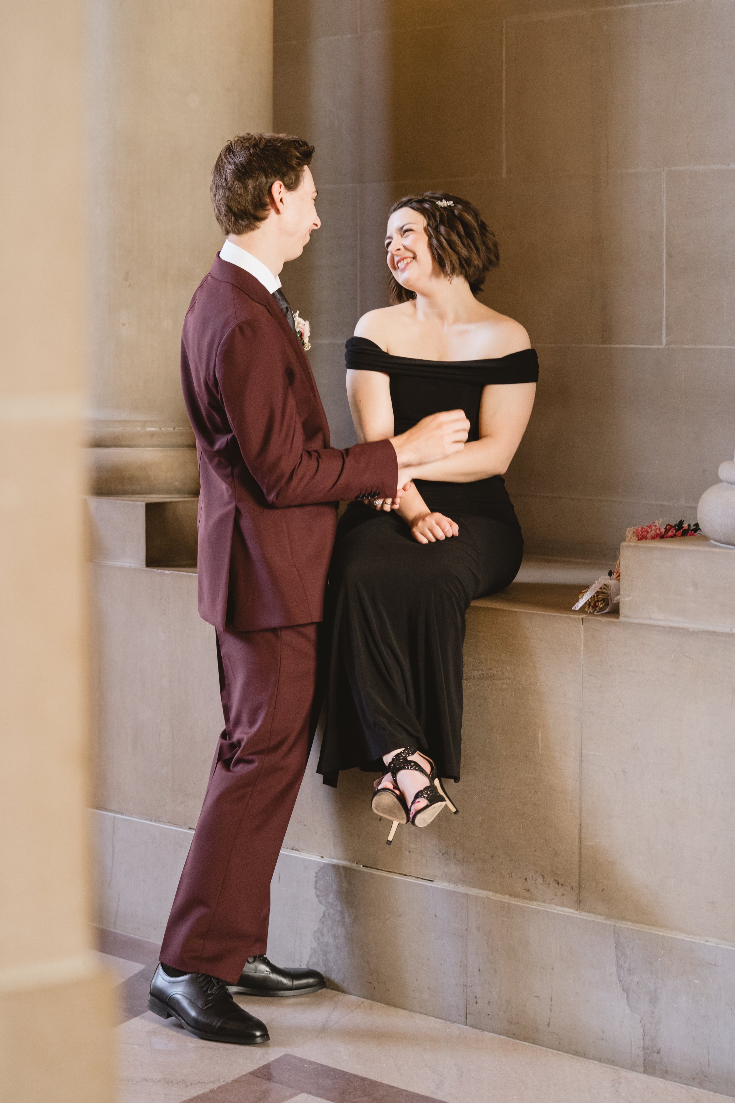 Bride laughing with groom on a stone ledge at City Hall