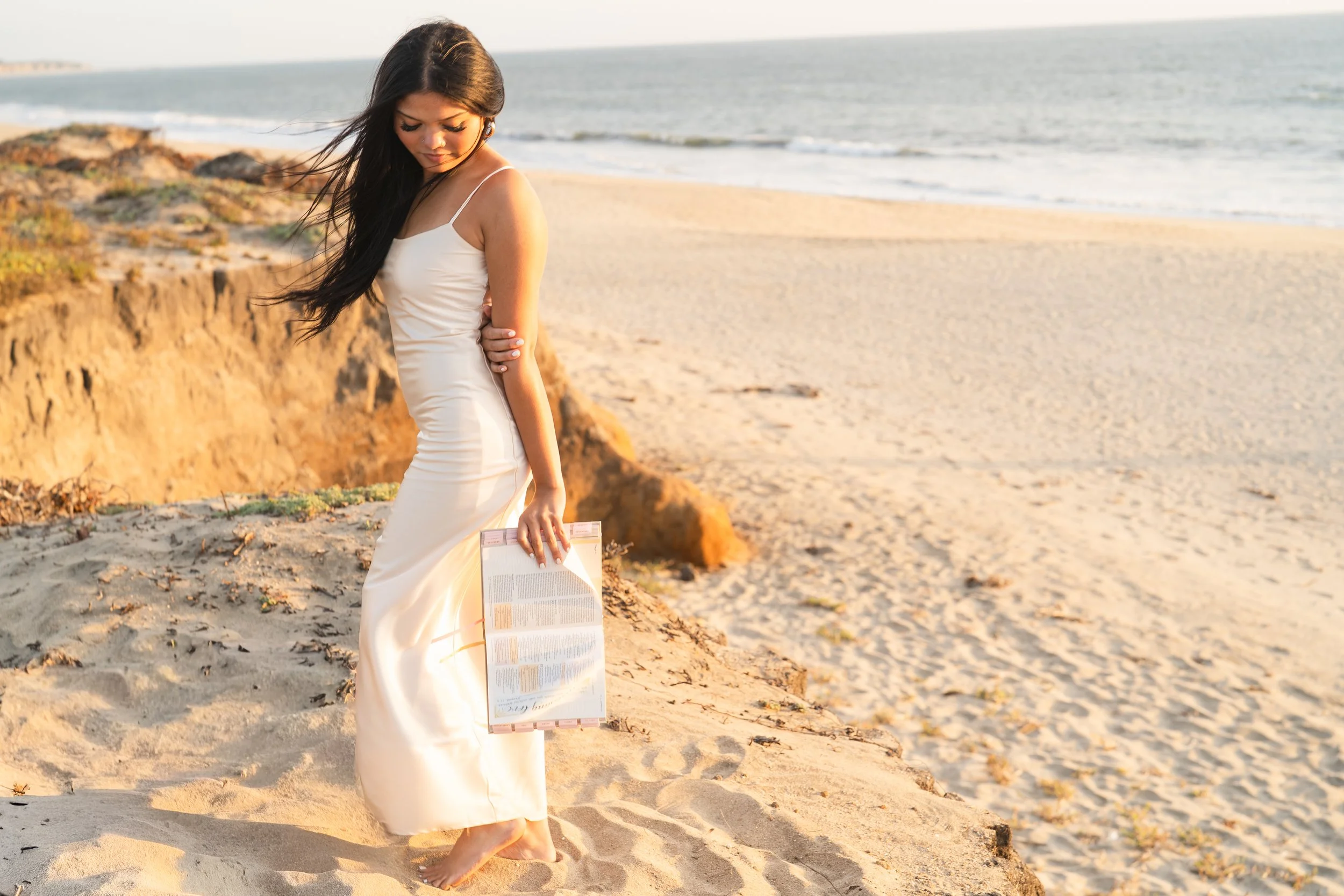 Senior holding her Bible and smiling over her shoulder on the dunes above a Half Moon Bay beach