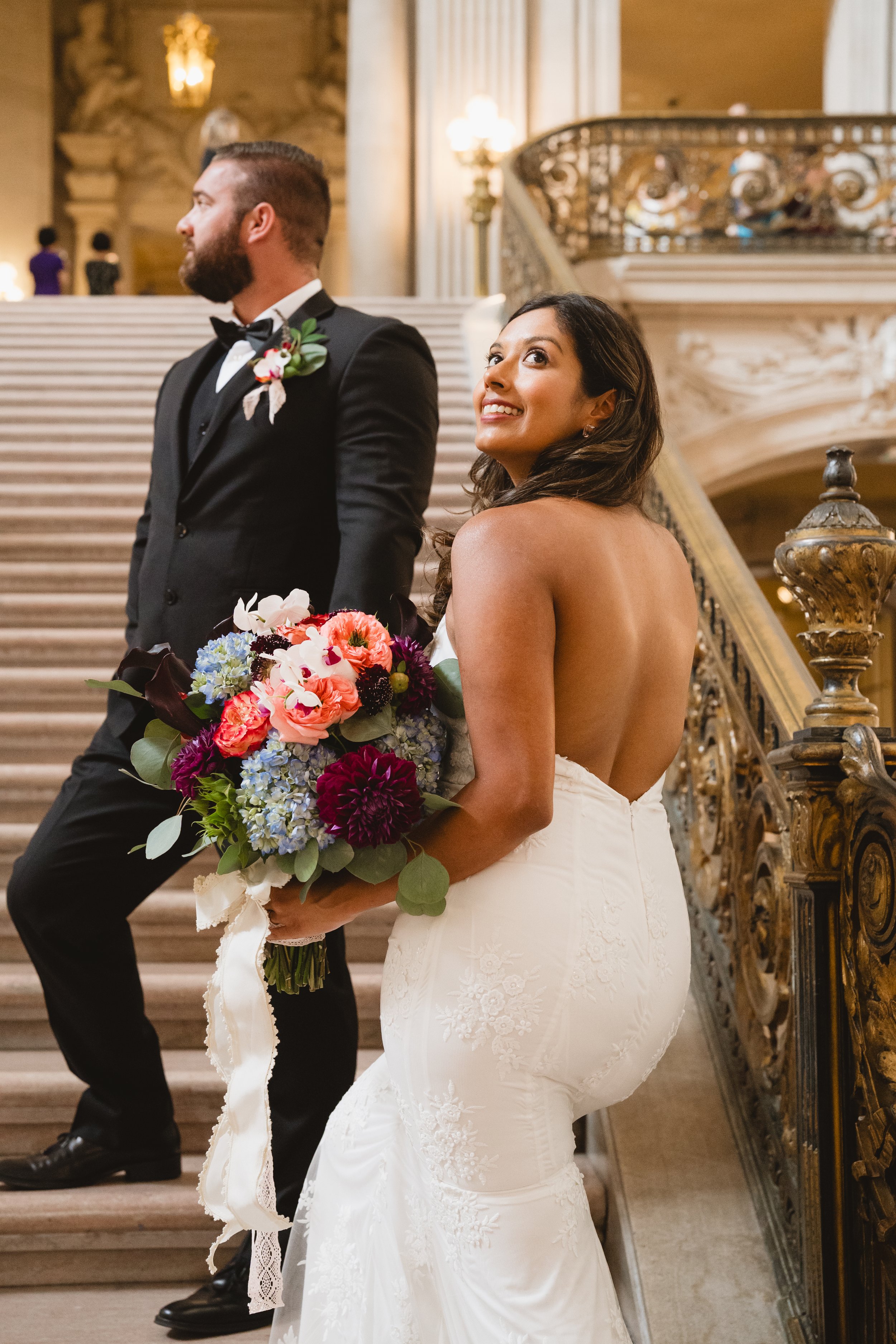 Bride glancing back over her shoulder on the Grand Staircase while her groom looks off to the side.