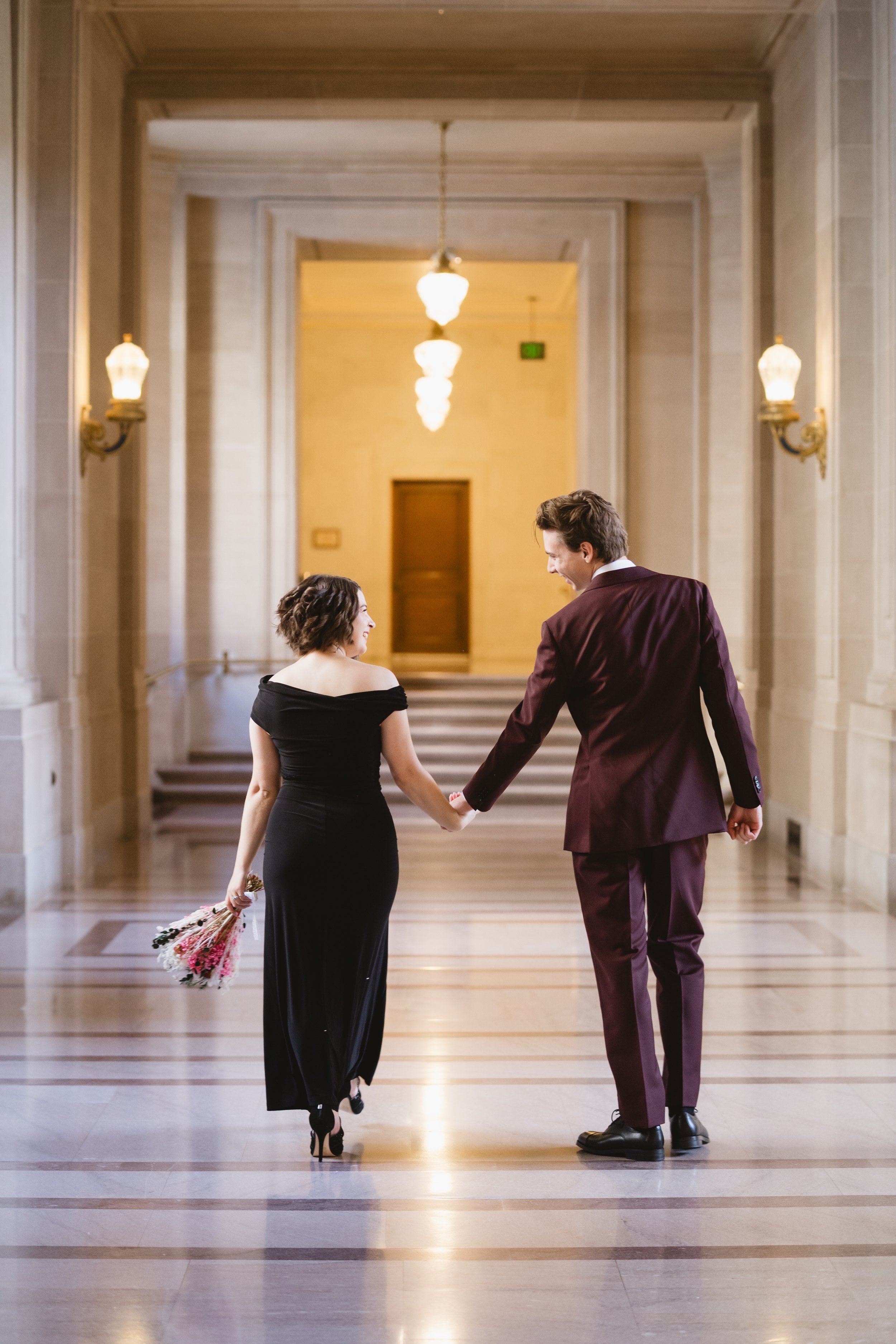 Couple holding hands in a sconce-lit hallway at San Francisco City Hall