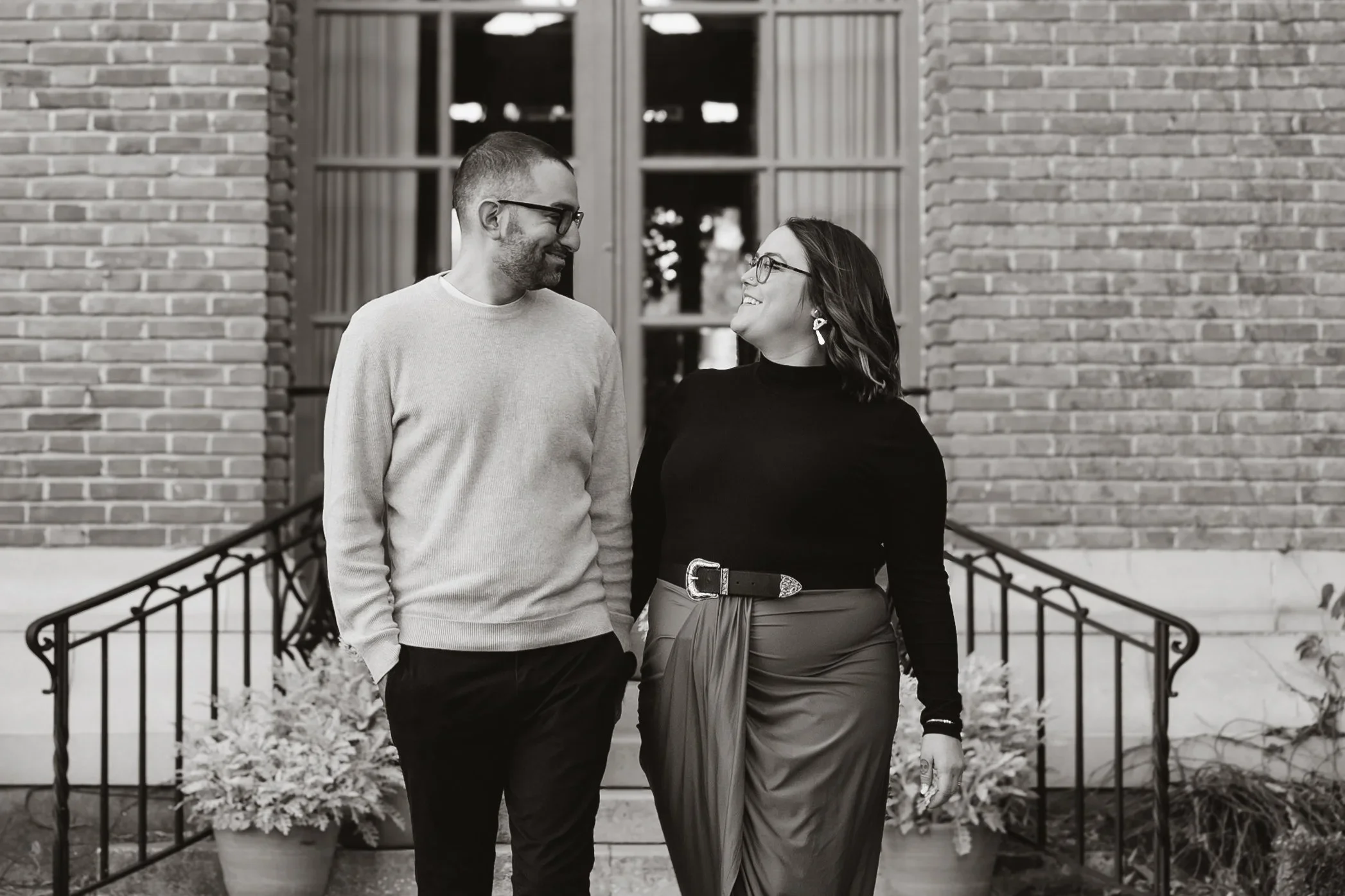 Engaged couple walking side by side away from the brick entry steps at Filoli, photographed in black and white, both dressed in soft neutrals.