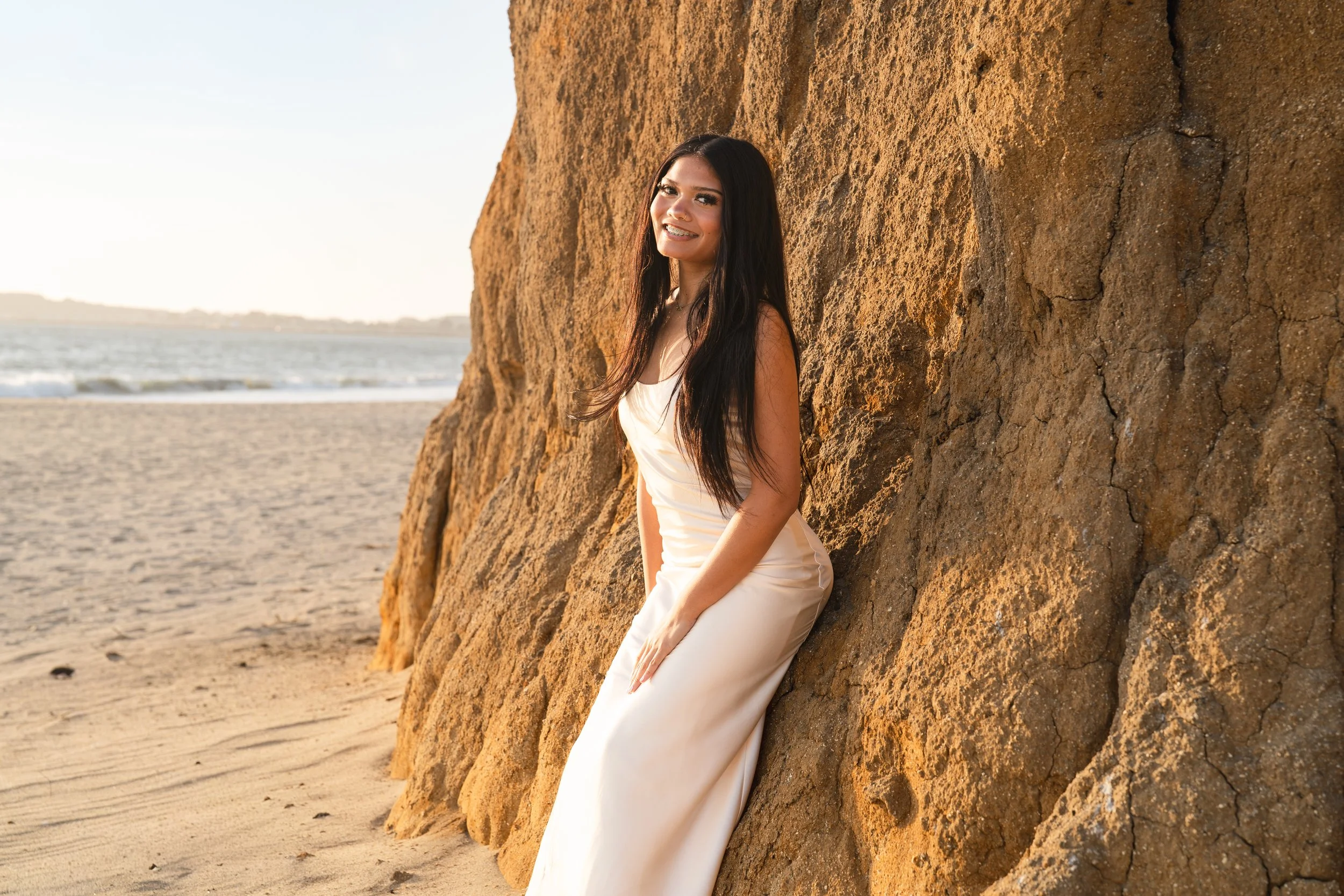 Senior leaning against a golden sandstone rock and smiling at the camera on a Half Moon Bay beach