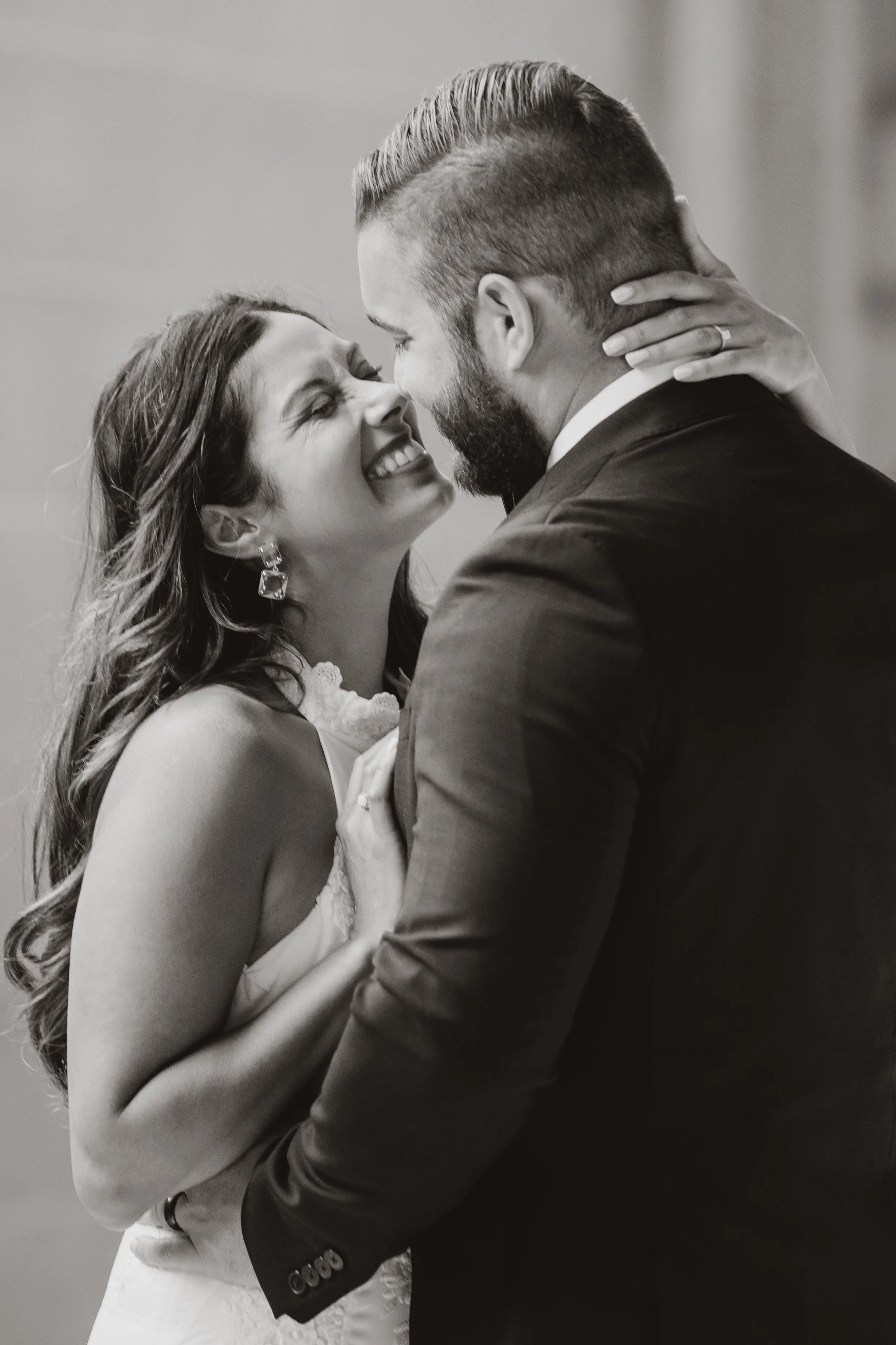 Black-and-white close-up of a groom cupping his bride's face as they smile at each other.