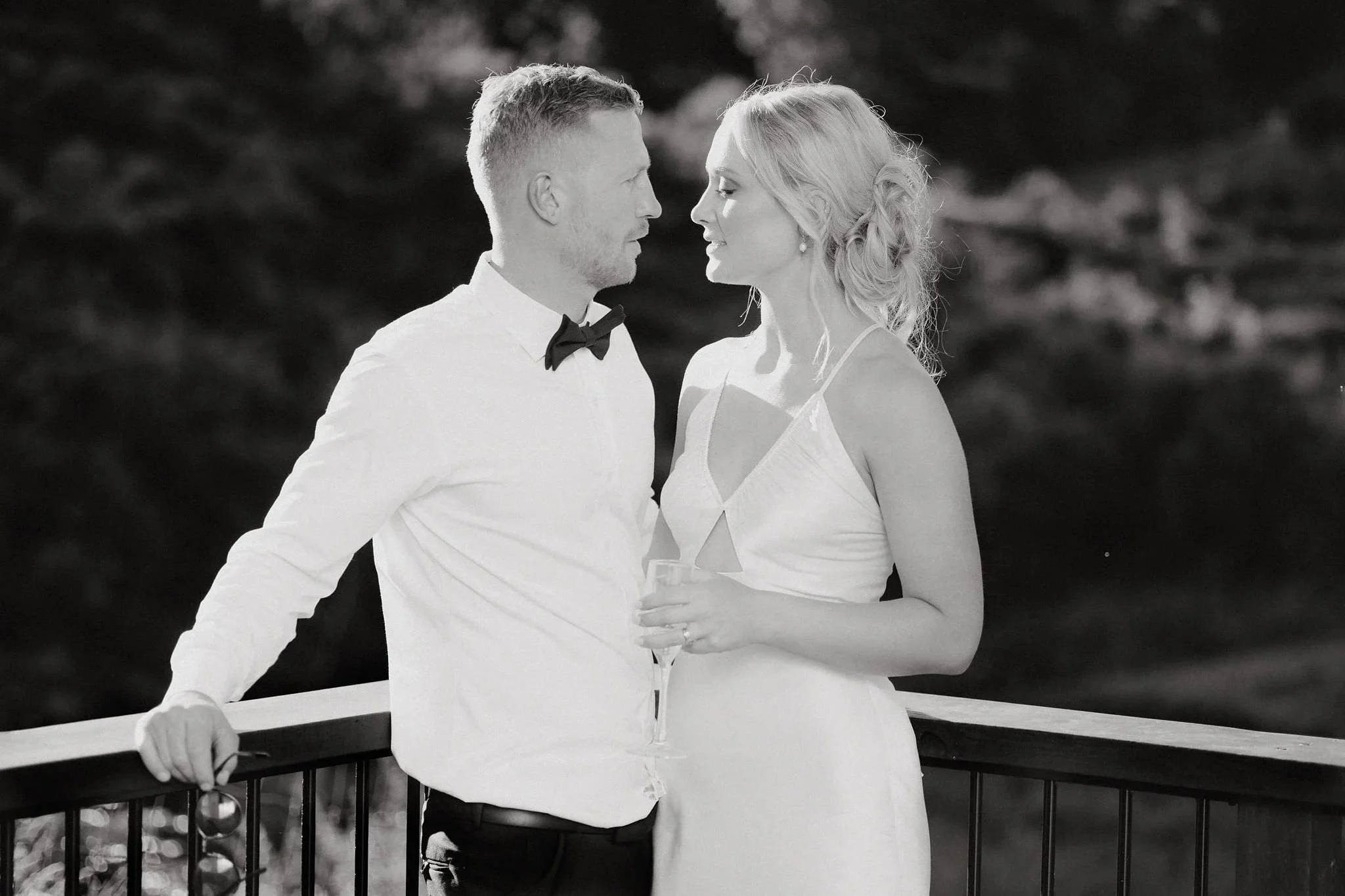 Classic black-and-white wedding photo of a couple gazing at each other on a balcony, showcasing soft light and documentary-style photography.