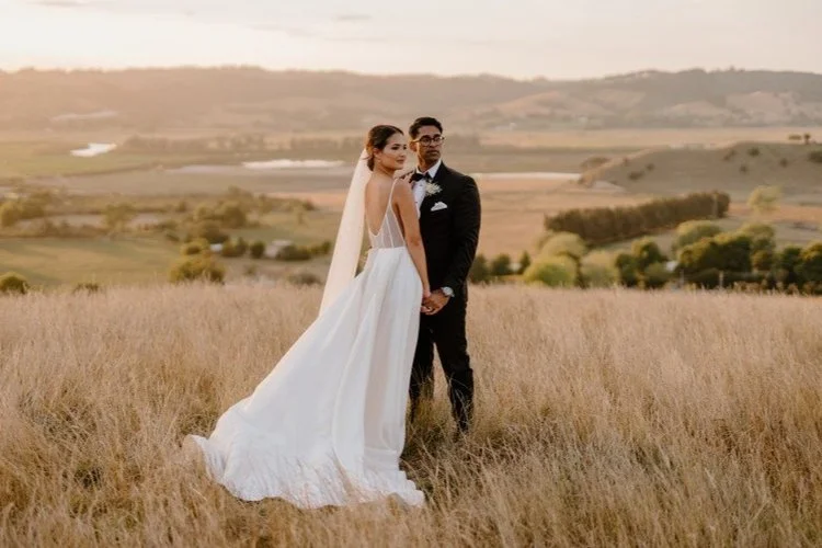 Sunset wedding portrait of a bride and groom in a golden field, framed by rolling rural landscapes and warm natural light.