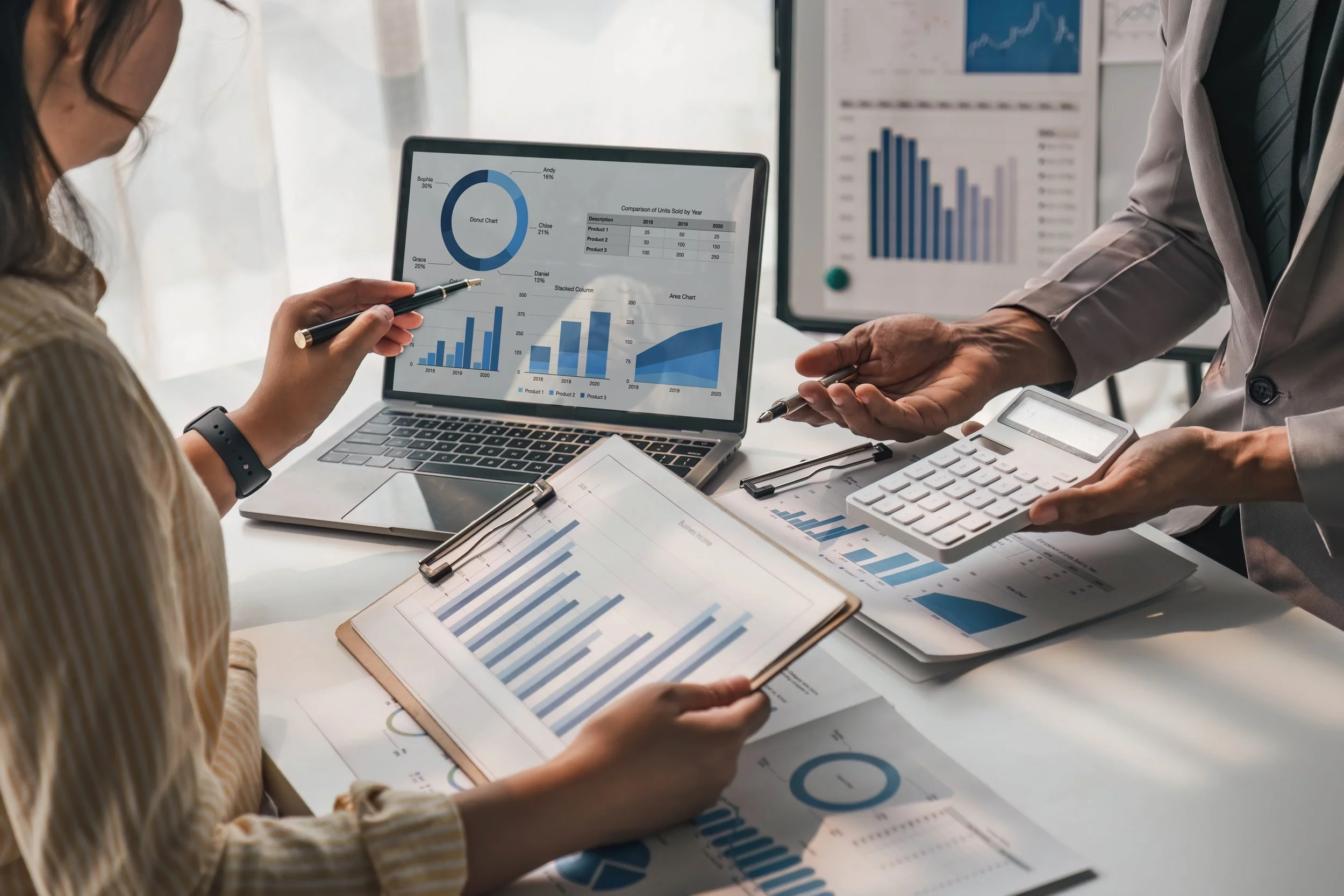 A magnifying glass, a calculator, and financial spreadsheets on a desk.